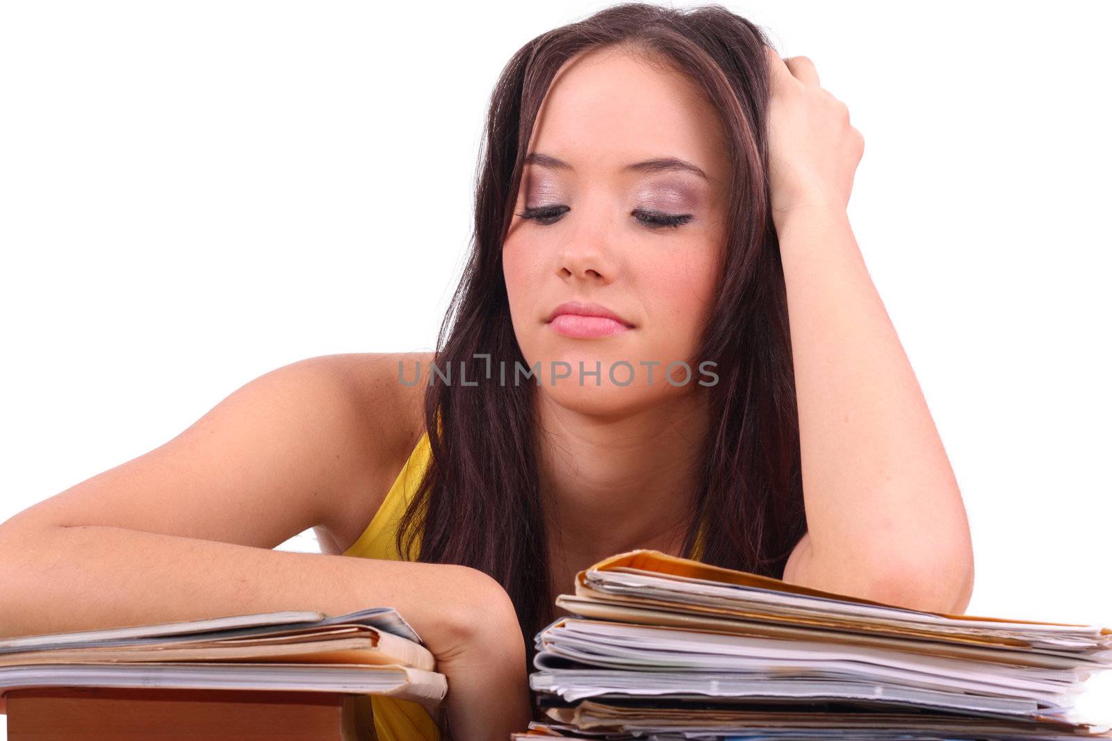 Stressed young woman sitting at a table among books and papers on a white background