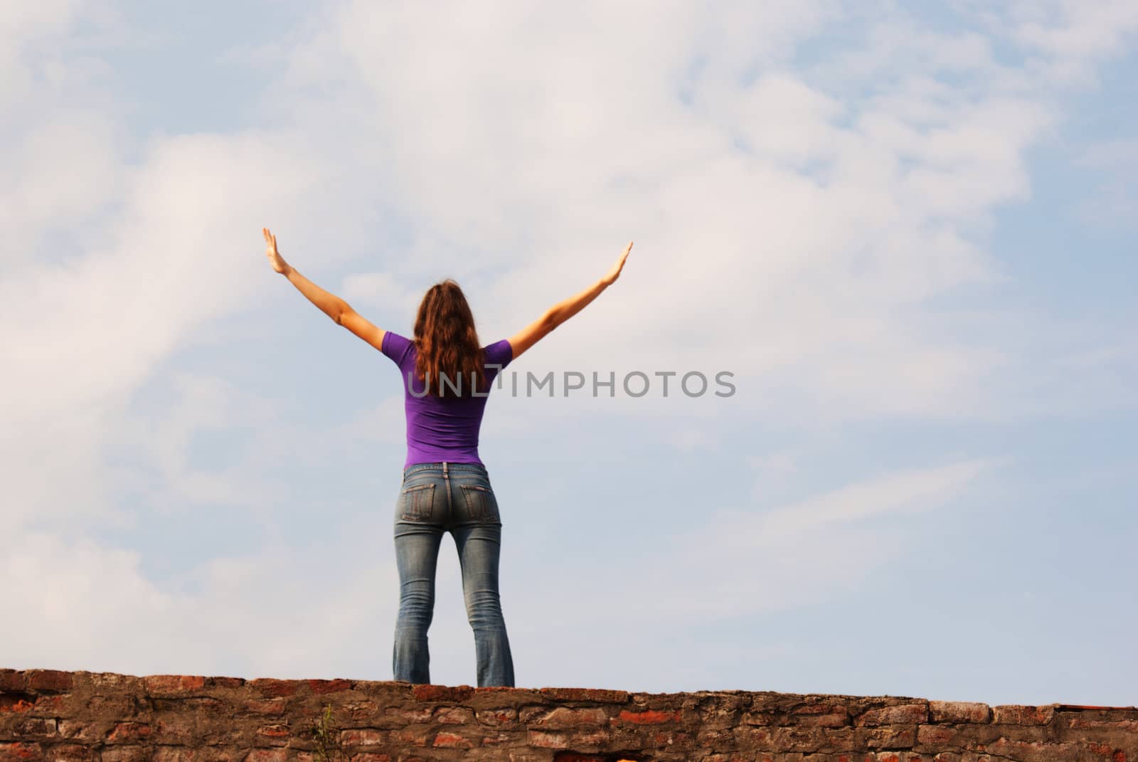 Young woman staying with raised hands against blue sky by AndreyKr
