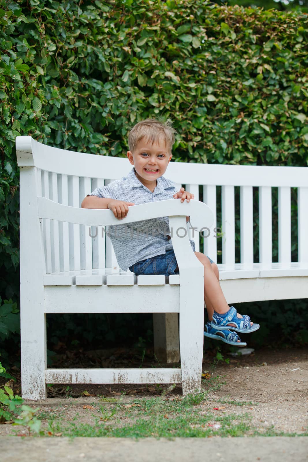 Cute little boy sits on a bench in a park. Vertical view