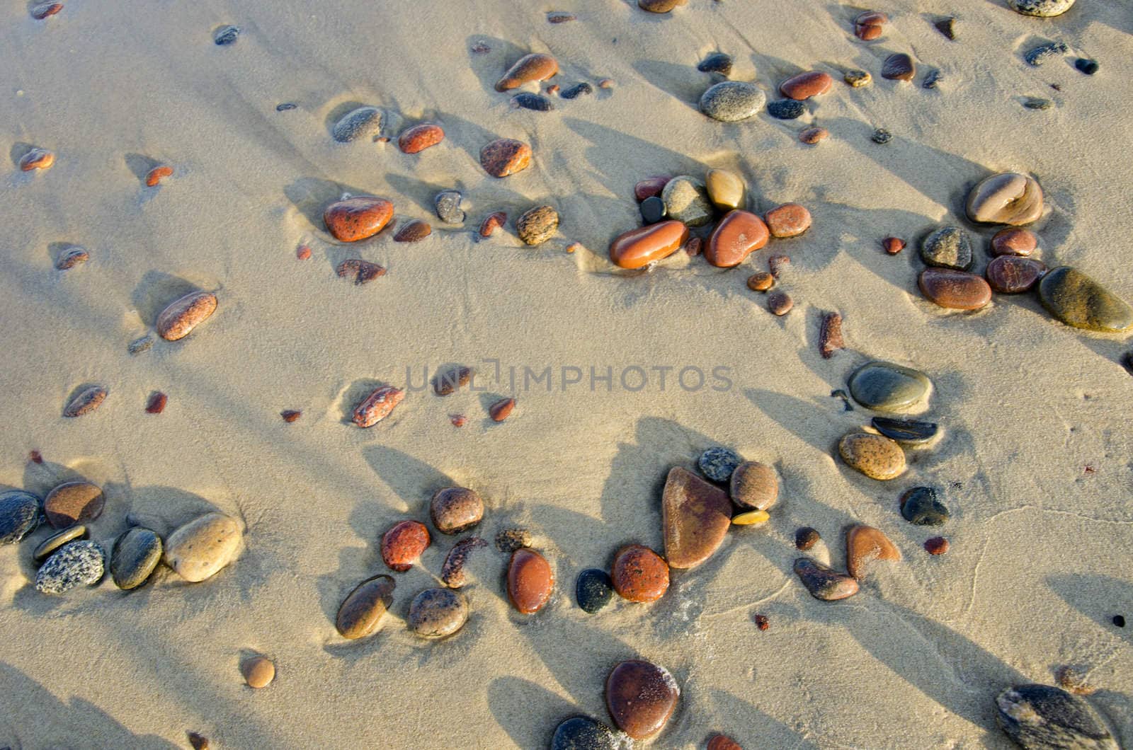 Colorful wet pebbles rubed by waves lying in sea sand.