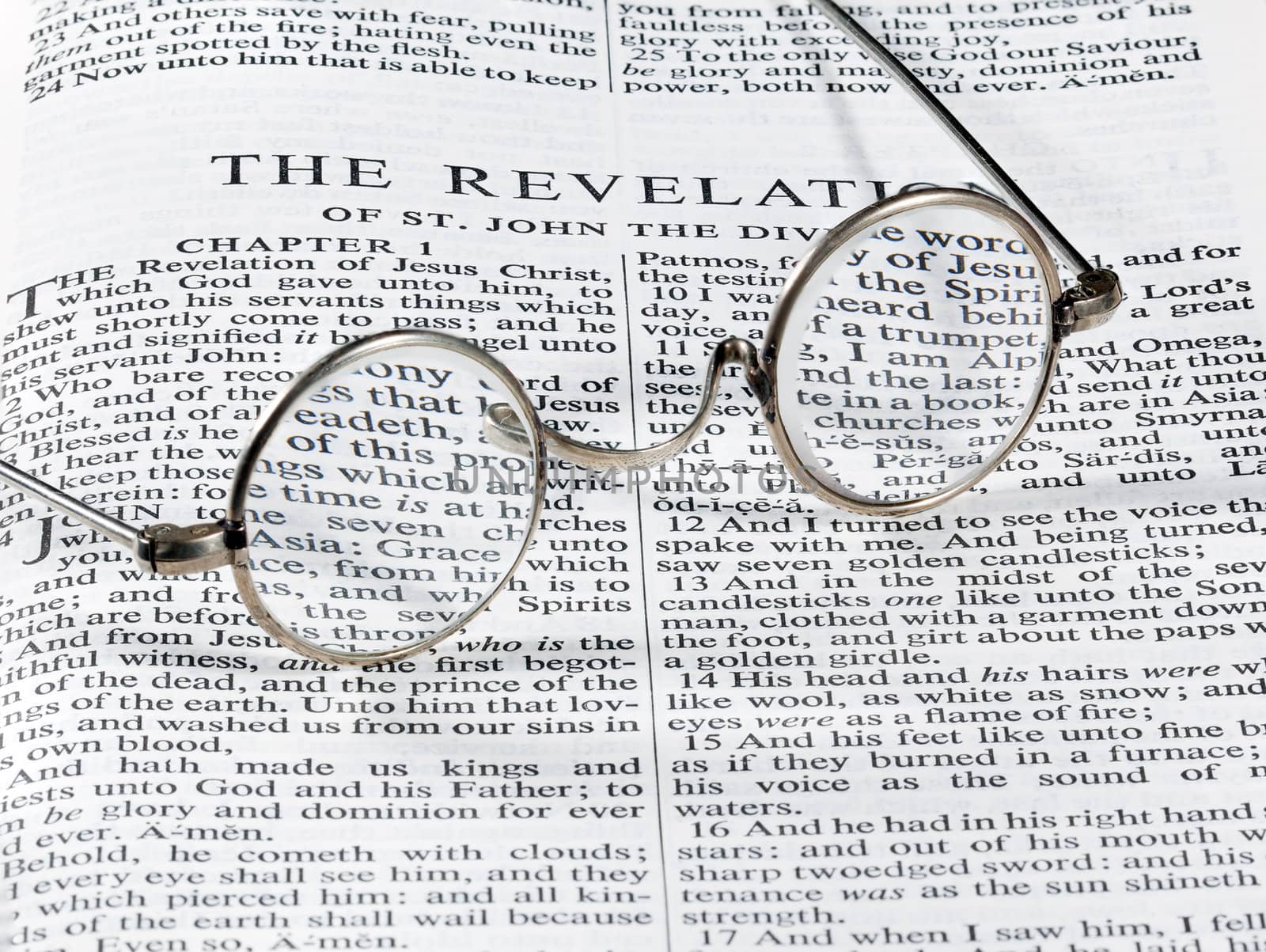 Old fashioned round reading glasses laying on a page from the bible on the revelation