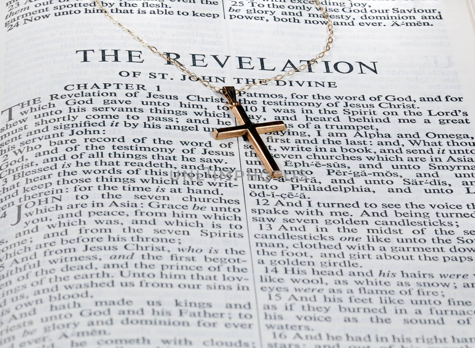 Old fashioned gold cross and chain laying on a page from the bible on the revelation