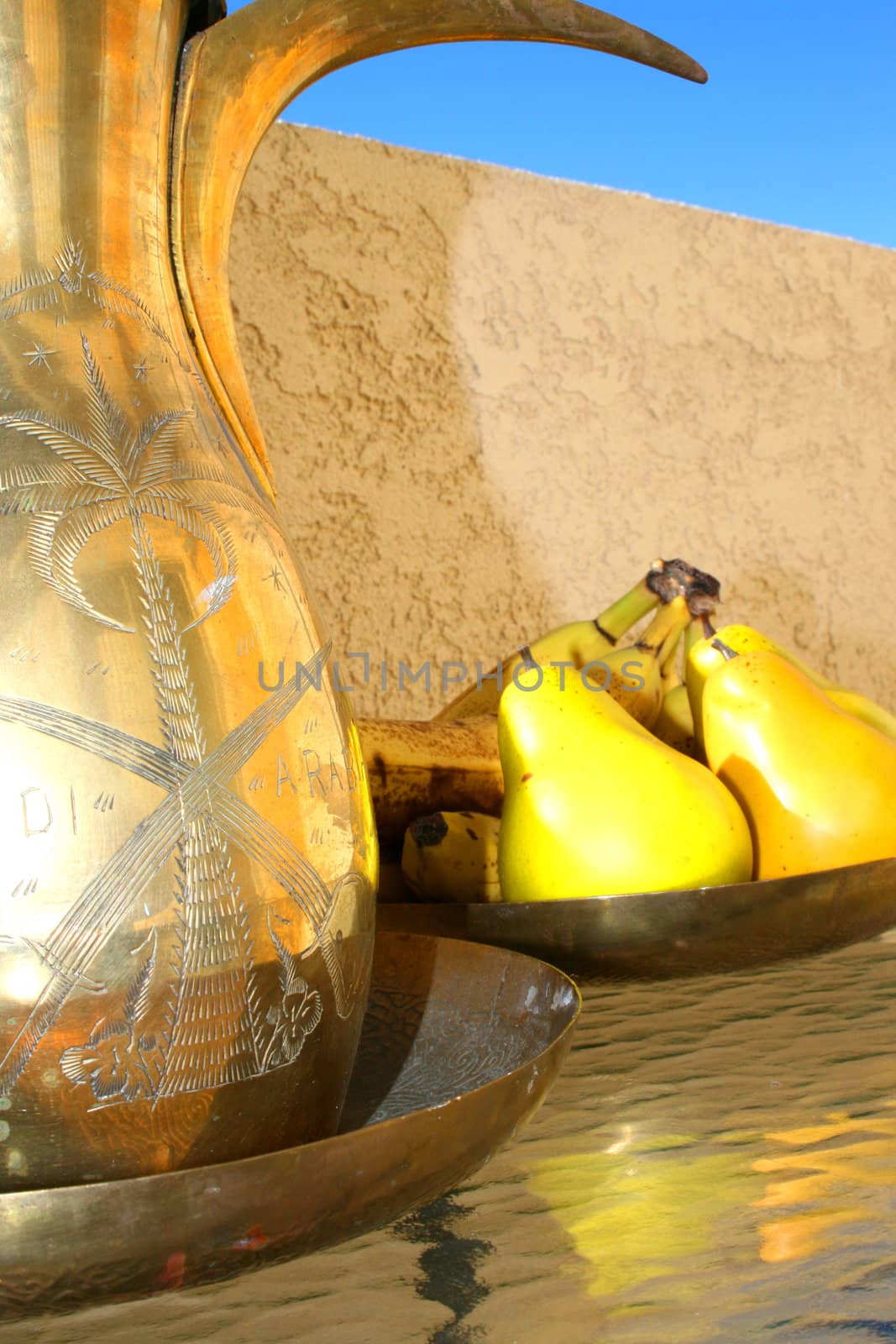 Brass olive oil decanter and a brass fruit bowl on a glass table.