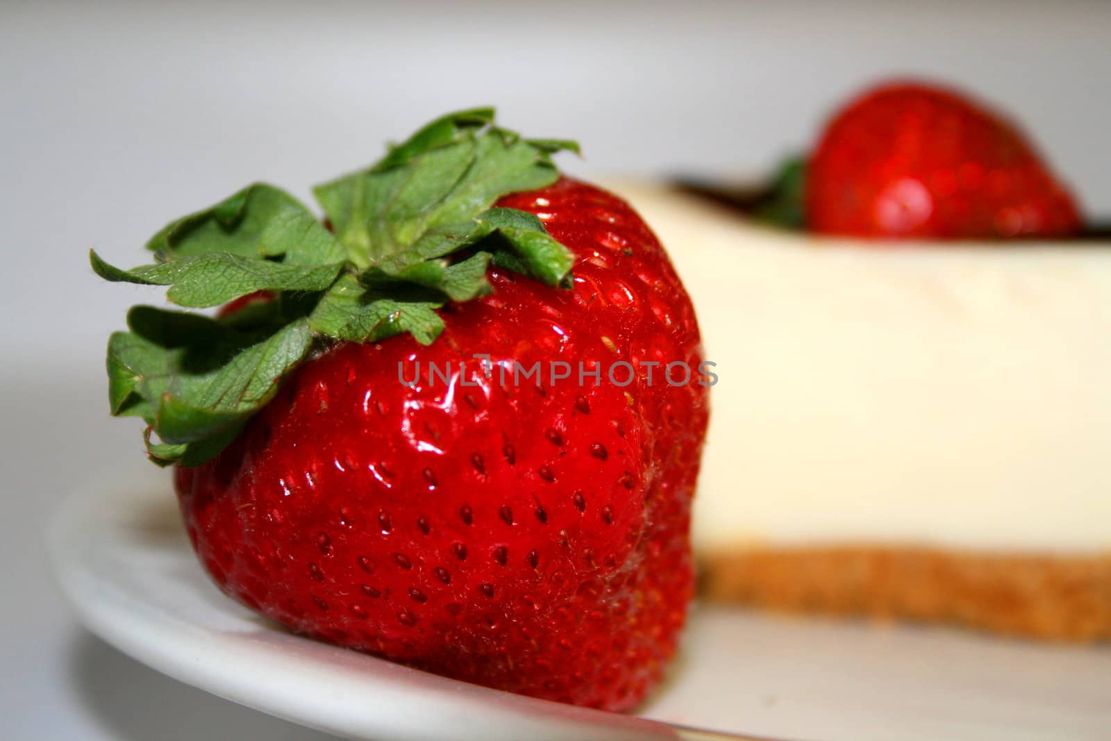 Close up of a strawberry and a cheesecake on a plate with a white background.