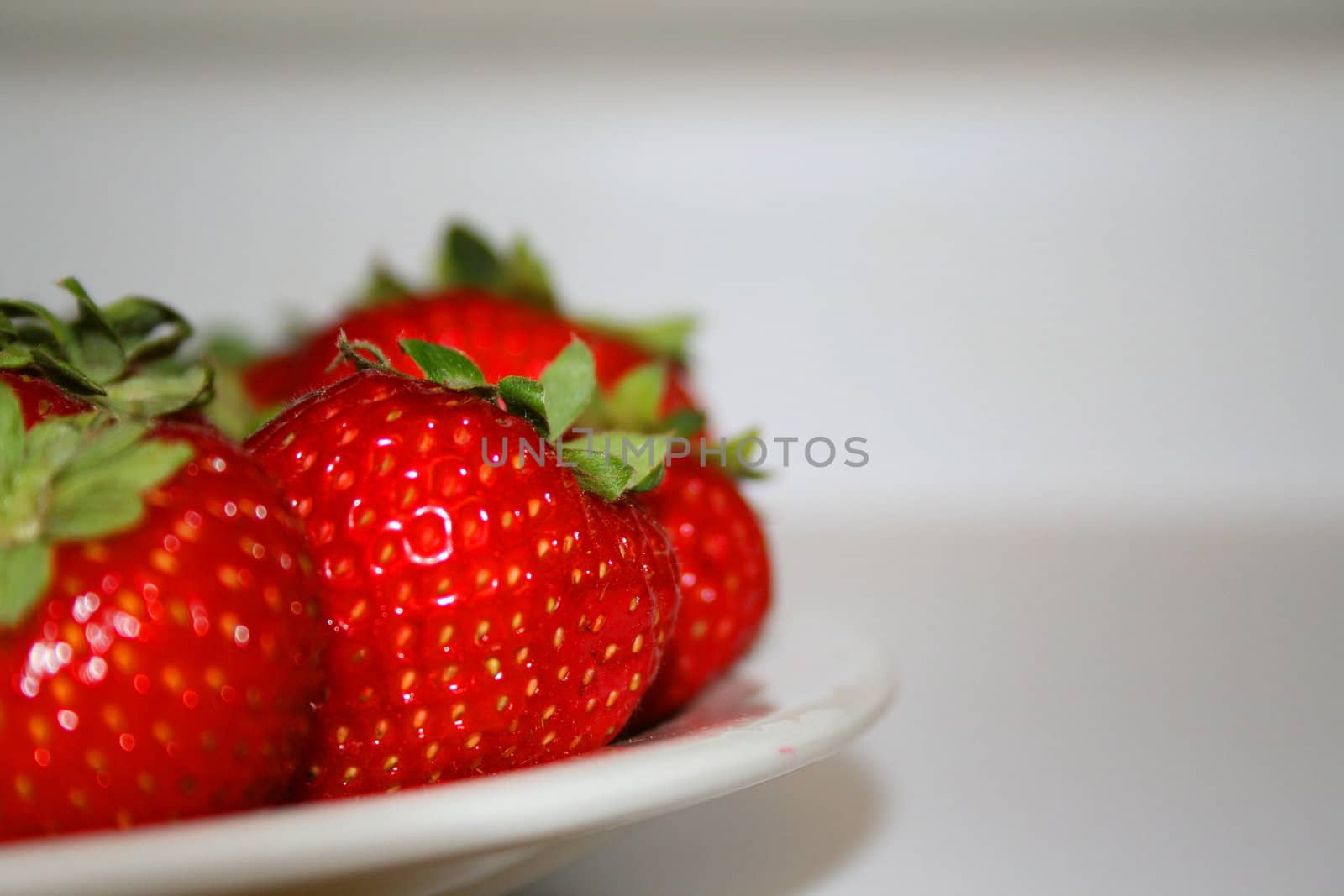 Close up of ripe strawberries on a plate with a white background.
