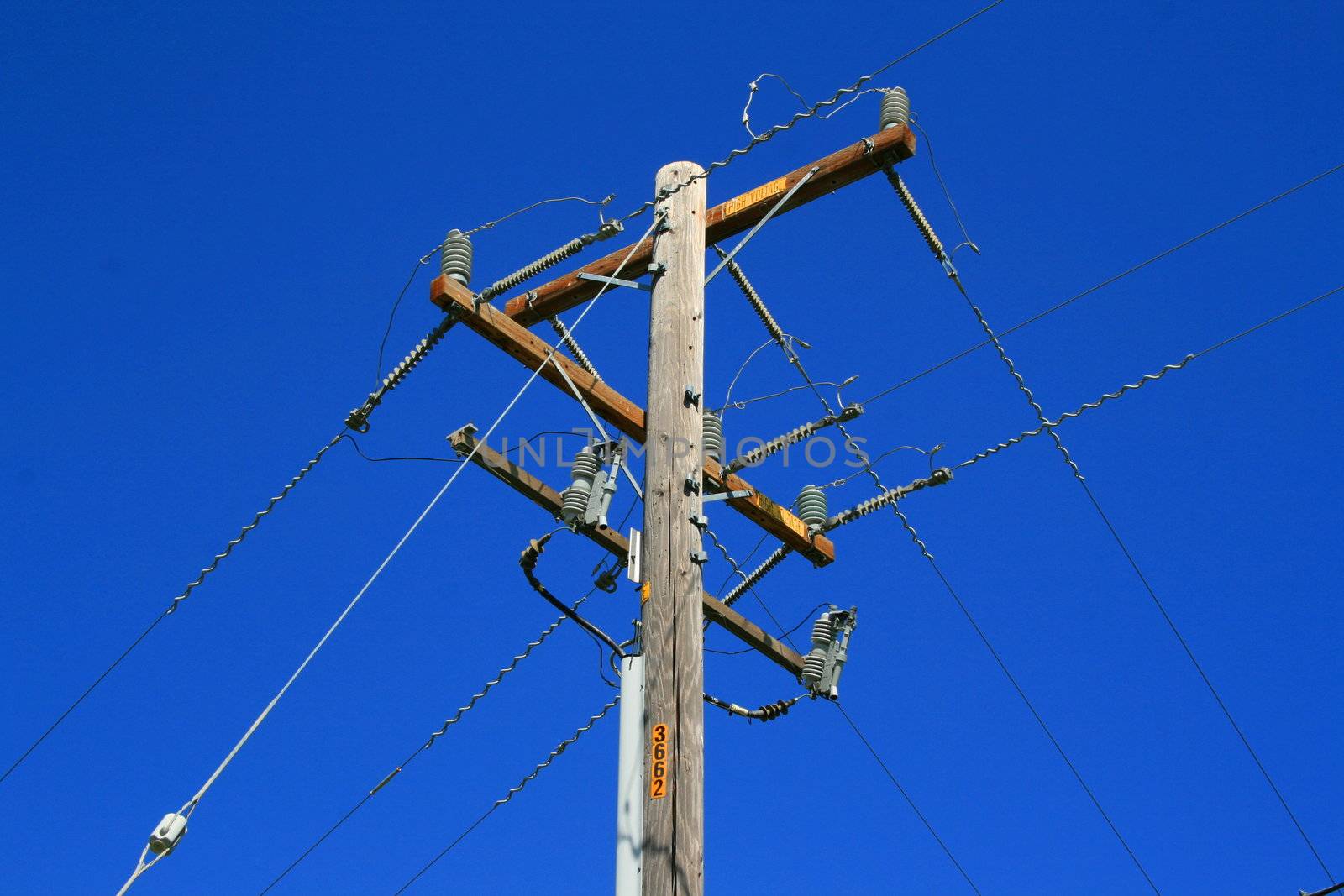 Close up of a telephone pole over blue sky.
