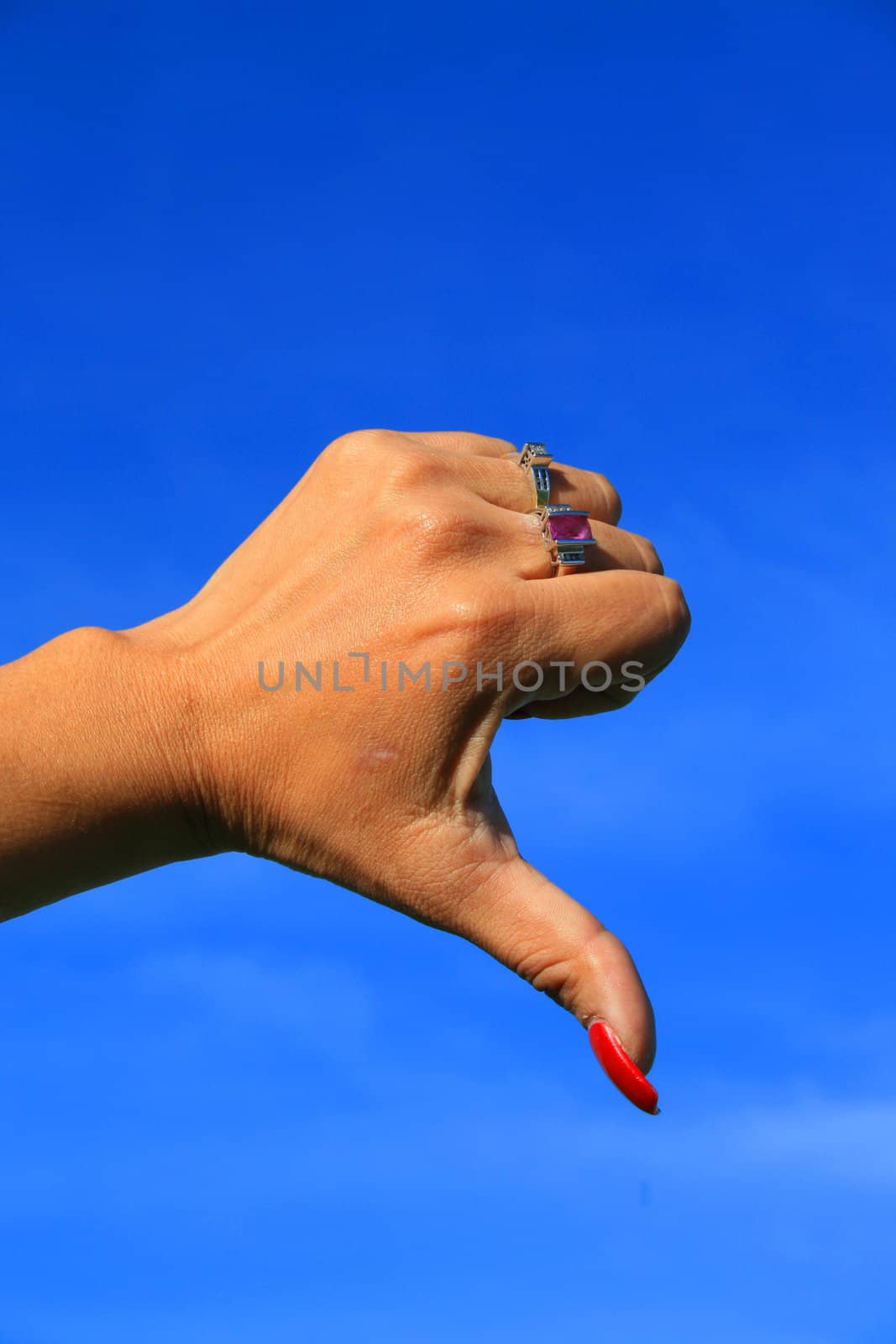 Woman's hand showing thumb down sign over blue sky.