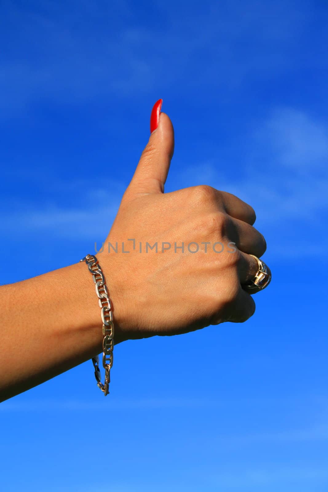 Woman's hand showing thumb up sign over blue sky.