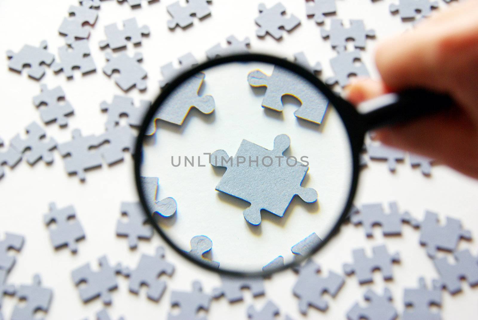Hand with magnifying glass and puzzle isolated on white background