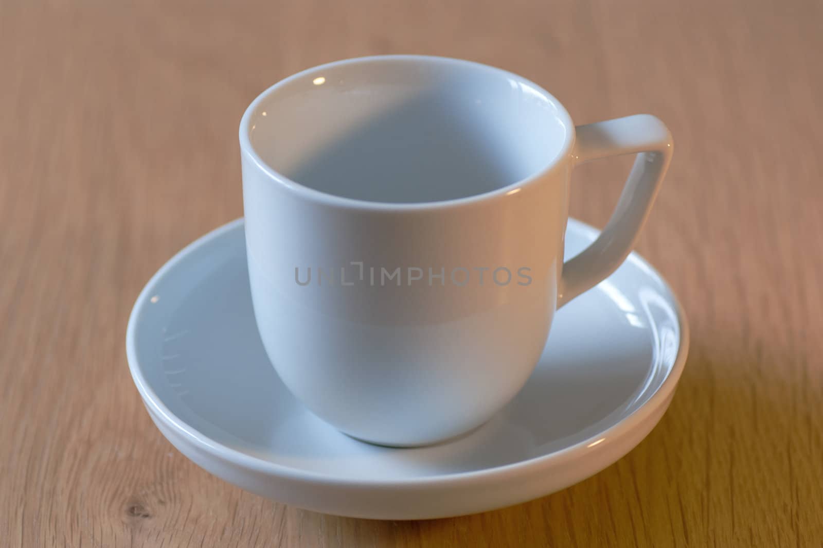 A white cup and saucer on an oak table top