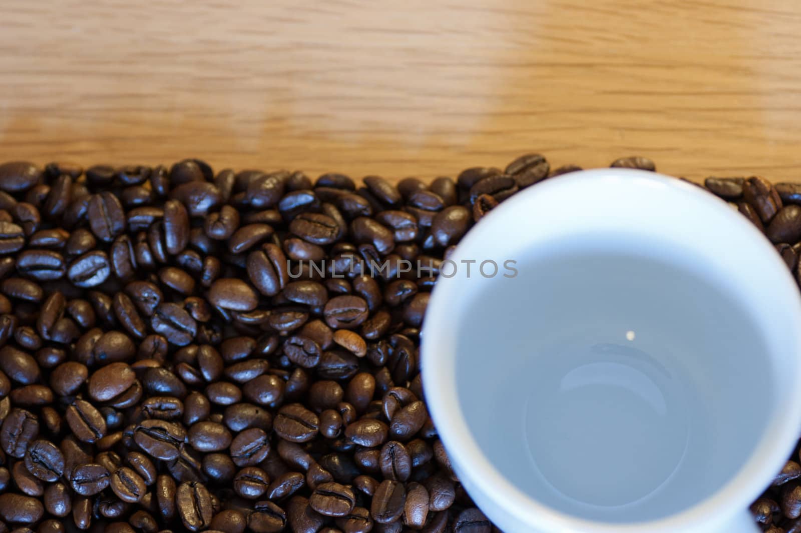 Dark roasted coffee beans on an oak table with a white cup