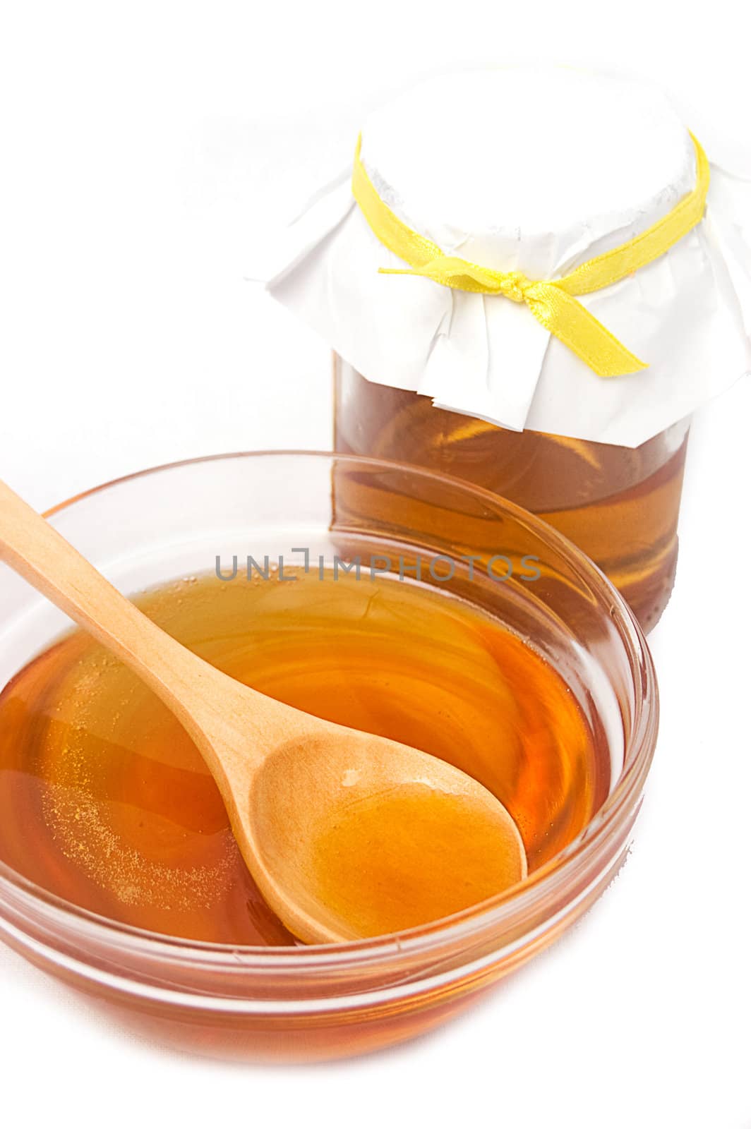 Honey jar with plate and wooden spoon over white