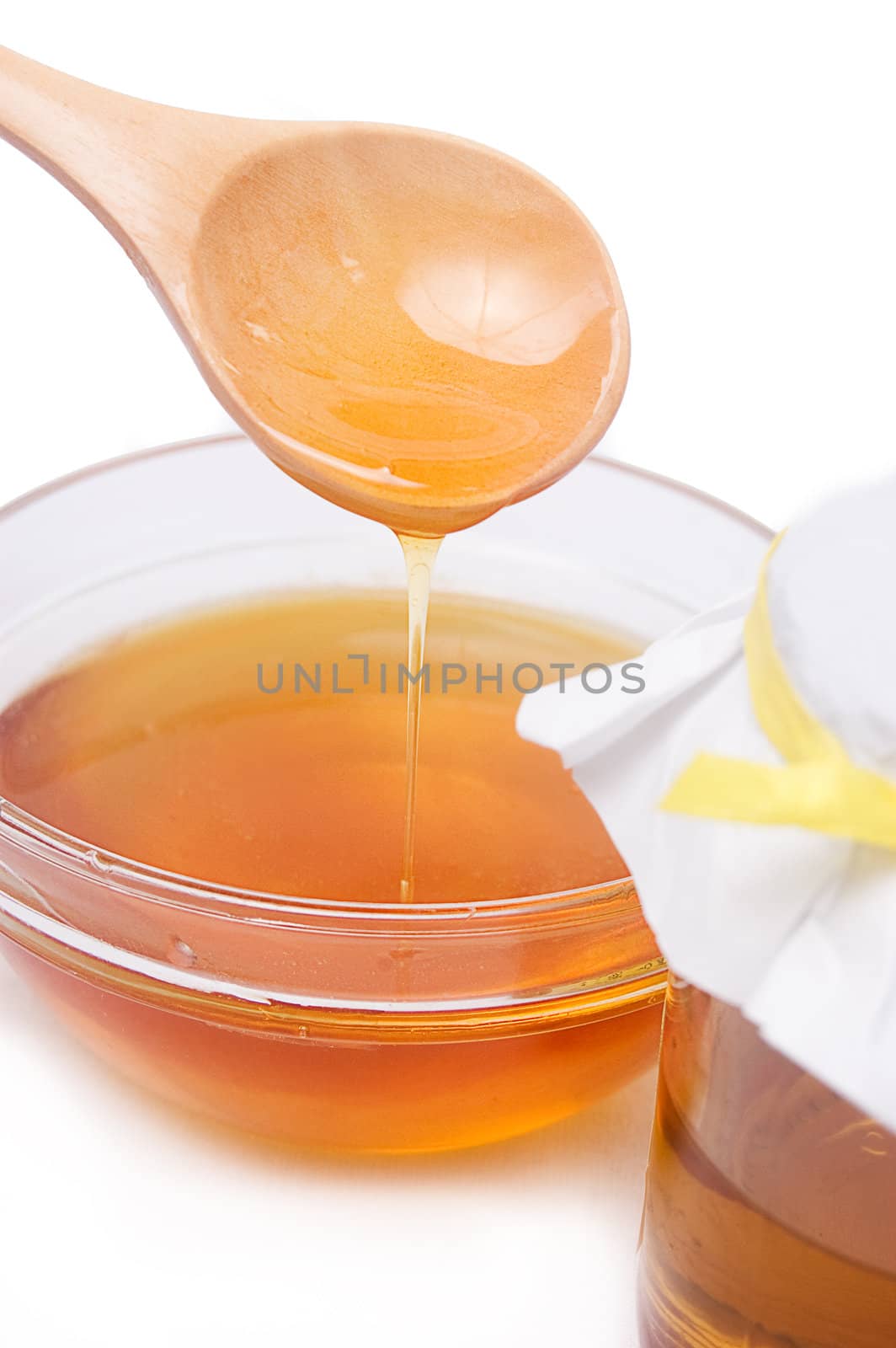 Honey running from wooden spoon in plate over white