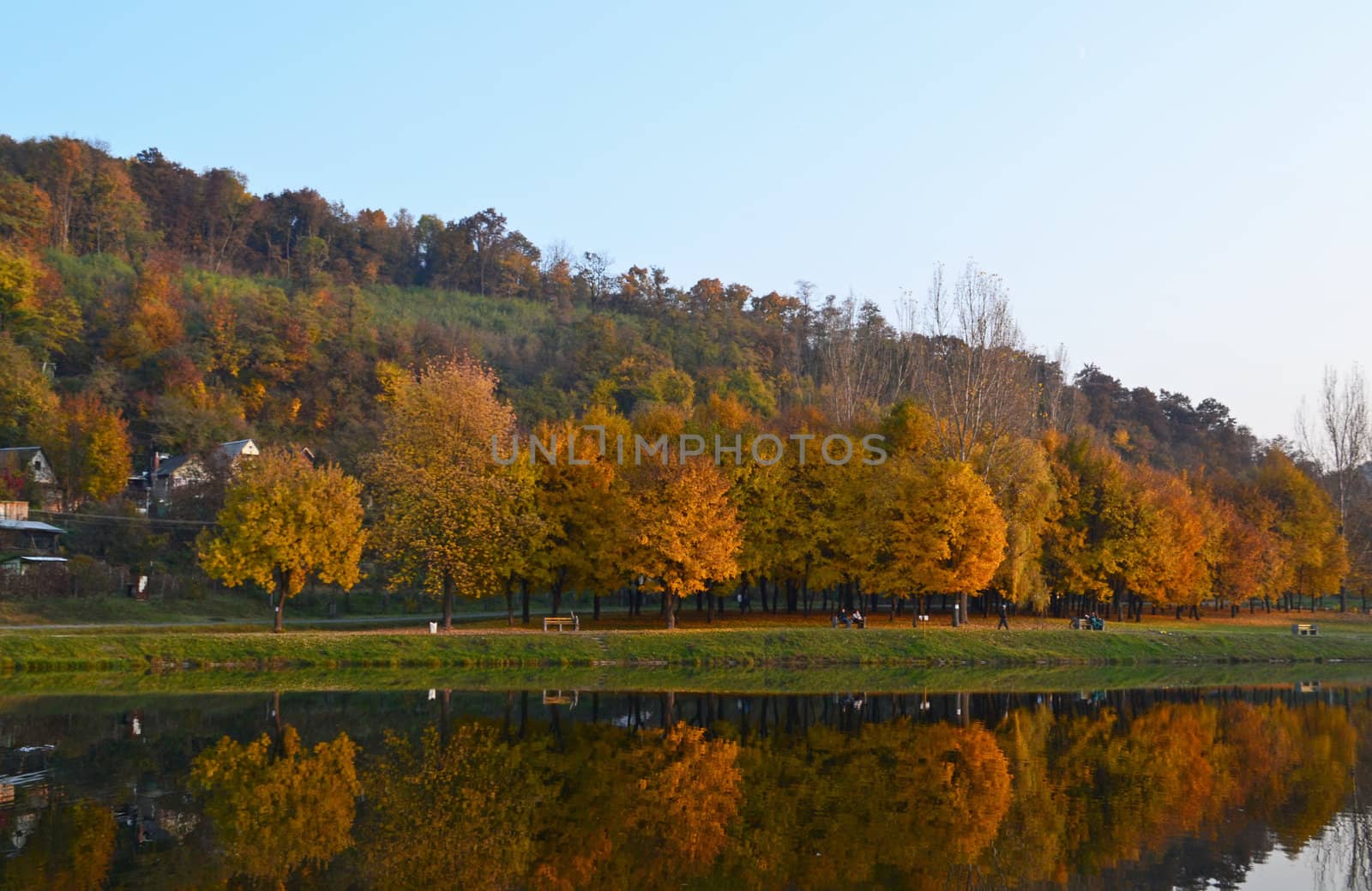 Small fishing lake in autumn, lit by the mellow late afternoon sunlight. Colors of foliage and reflections on the calm water surface are beautiful, yet create a gloomy atmosphere. Residents of the nearby town take a rest on the lakeside fishing, or just relaxing.