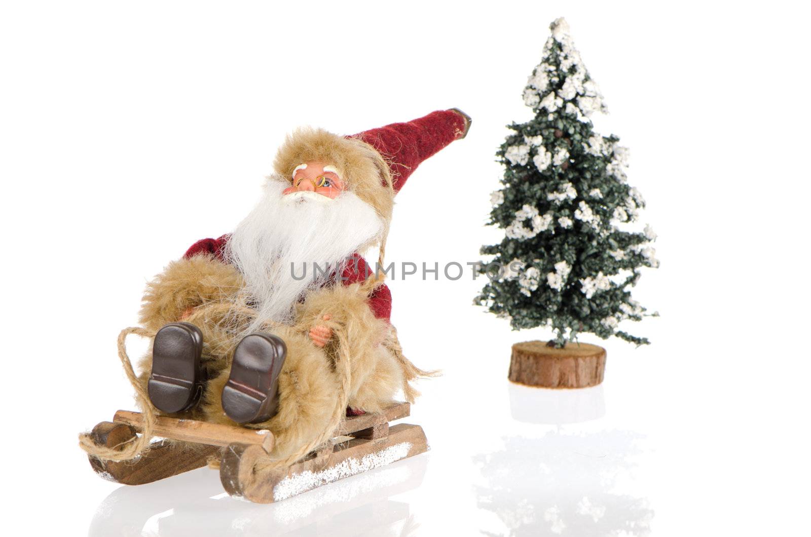 Miniature of Santa Claus on sleigh and a pine tree with snow, on white reflective background.