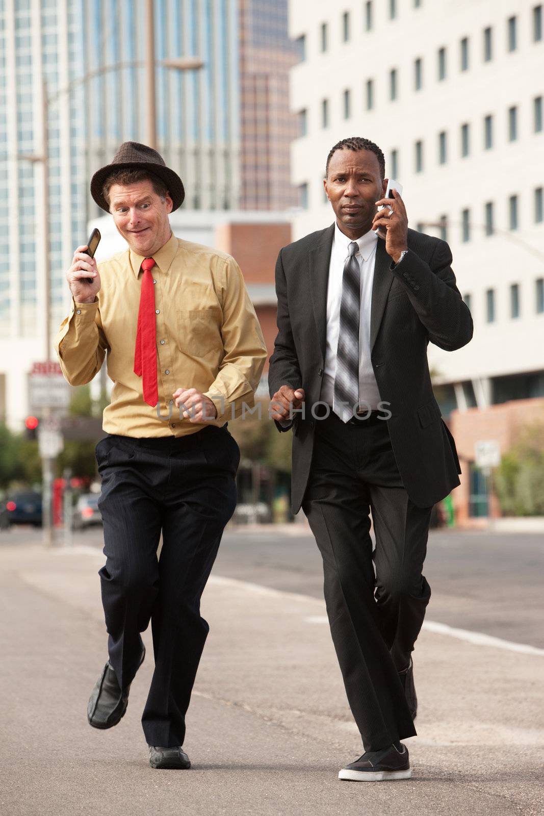 Two businessmen on phones rush down the street