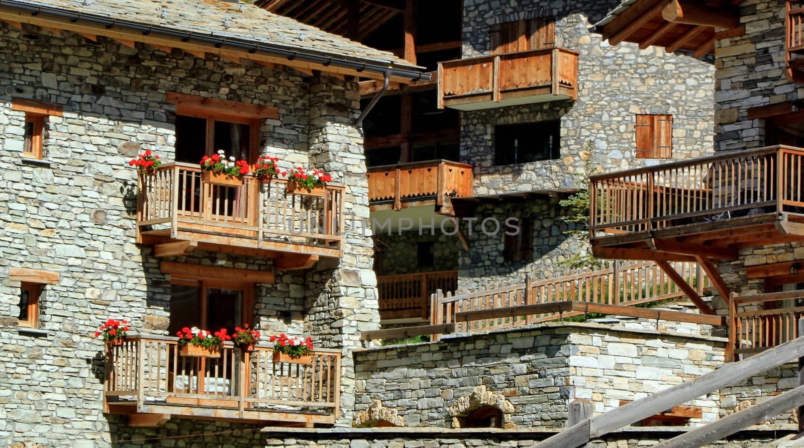 Close up of chalets made of grey stones and with red flowers on balconies by summer, Val d'Isere, France