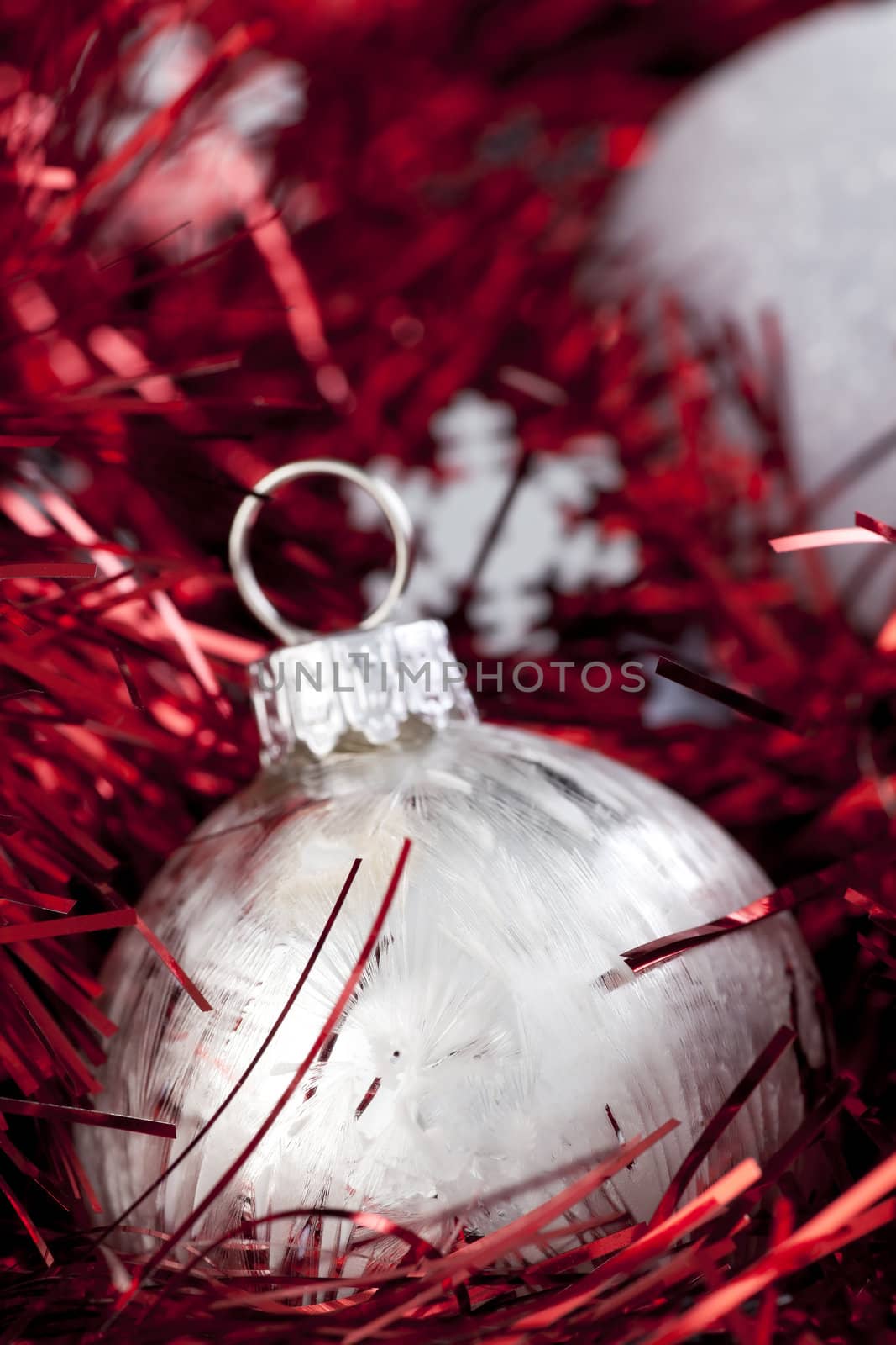 Silver Christmas ball ornament sitting in red garland with silver snowflake shapes.