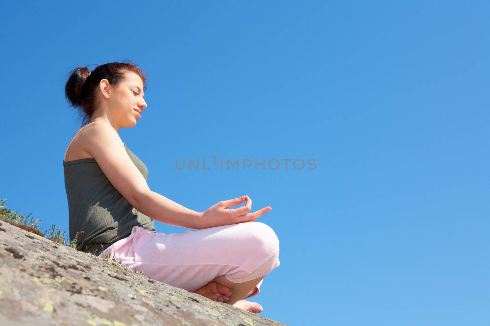 Teenage girl meditating on rock, side view