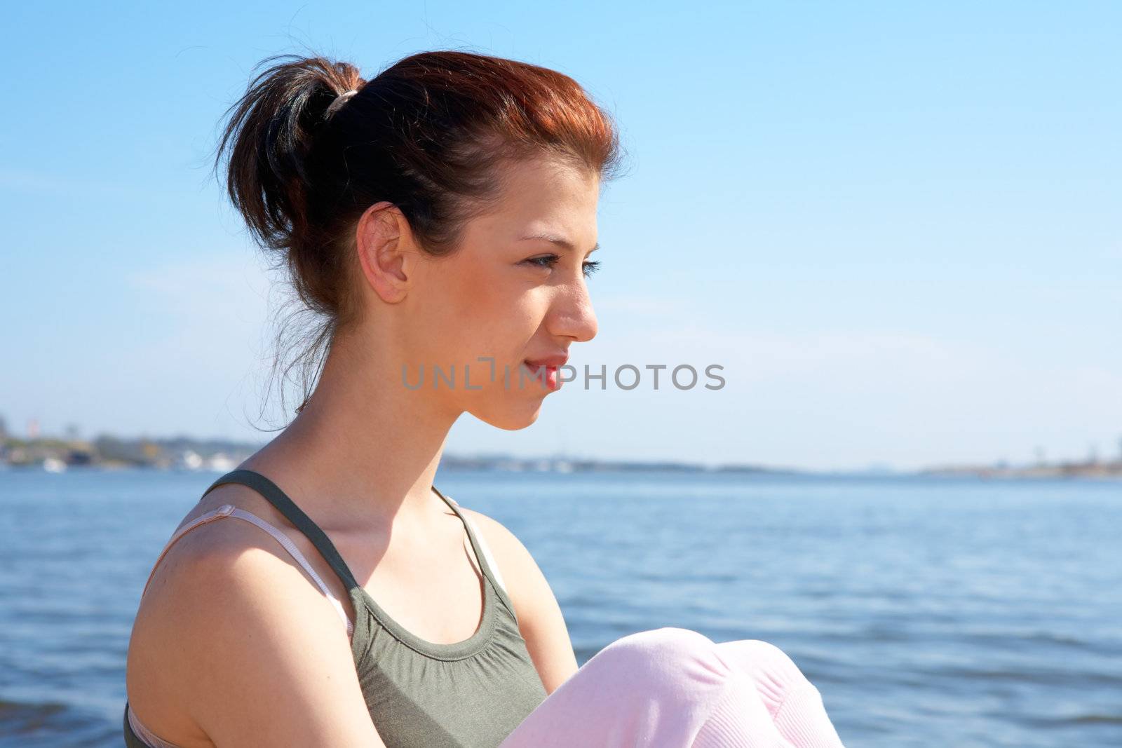 Teenage girl sitting by sea on sunny day, looking away
