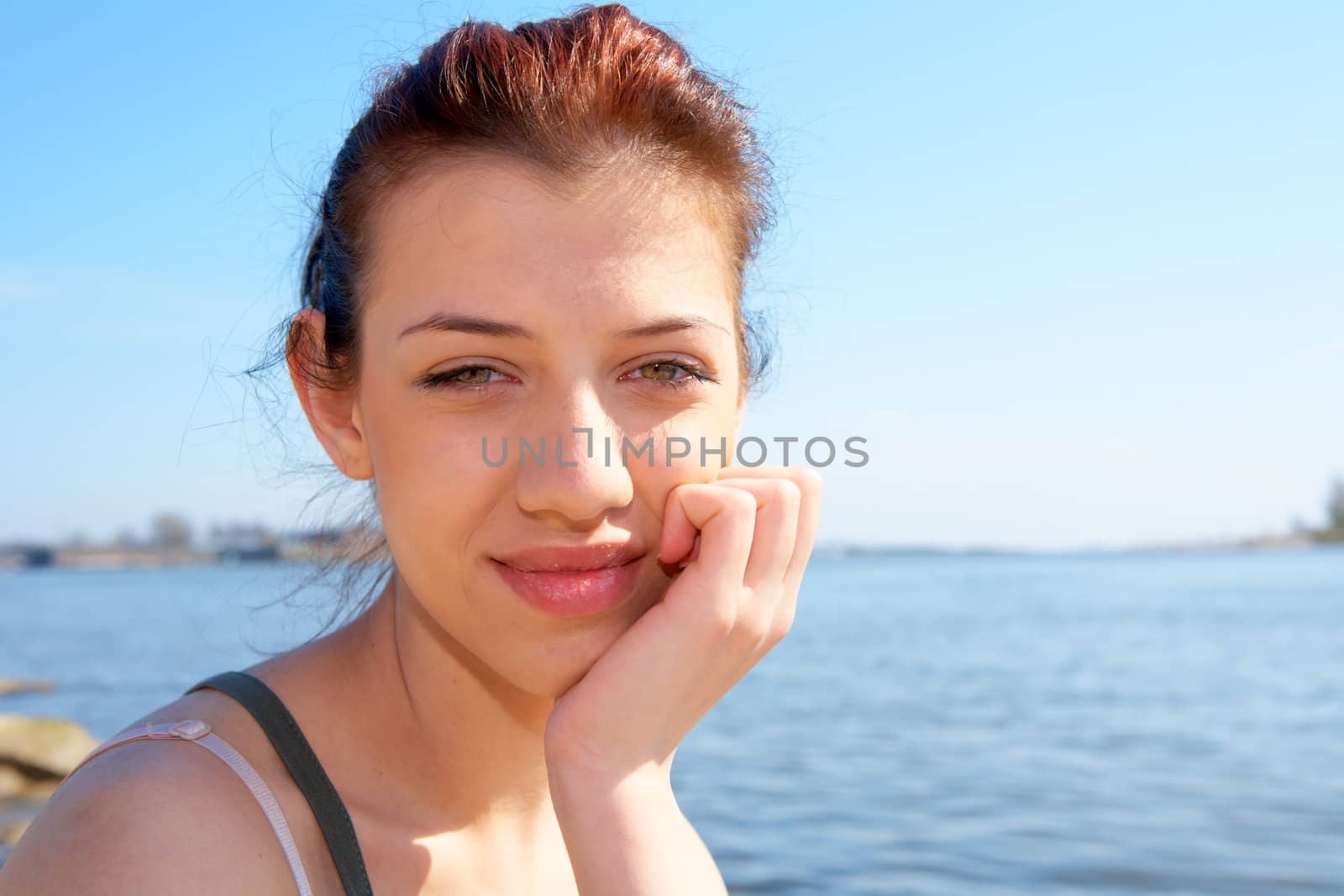 Teenage girl sitting by sea on sunny day holding chin