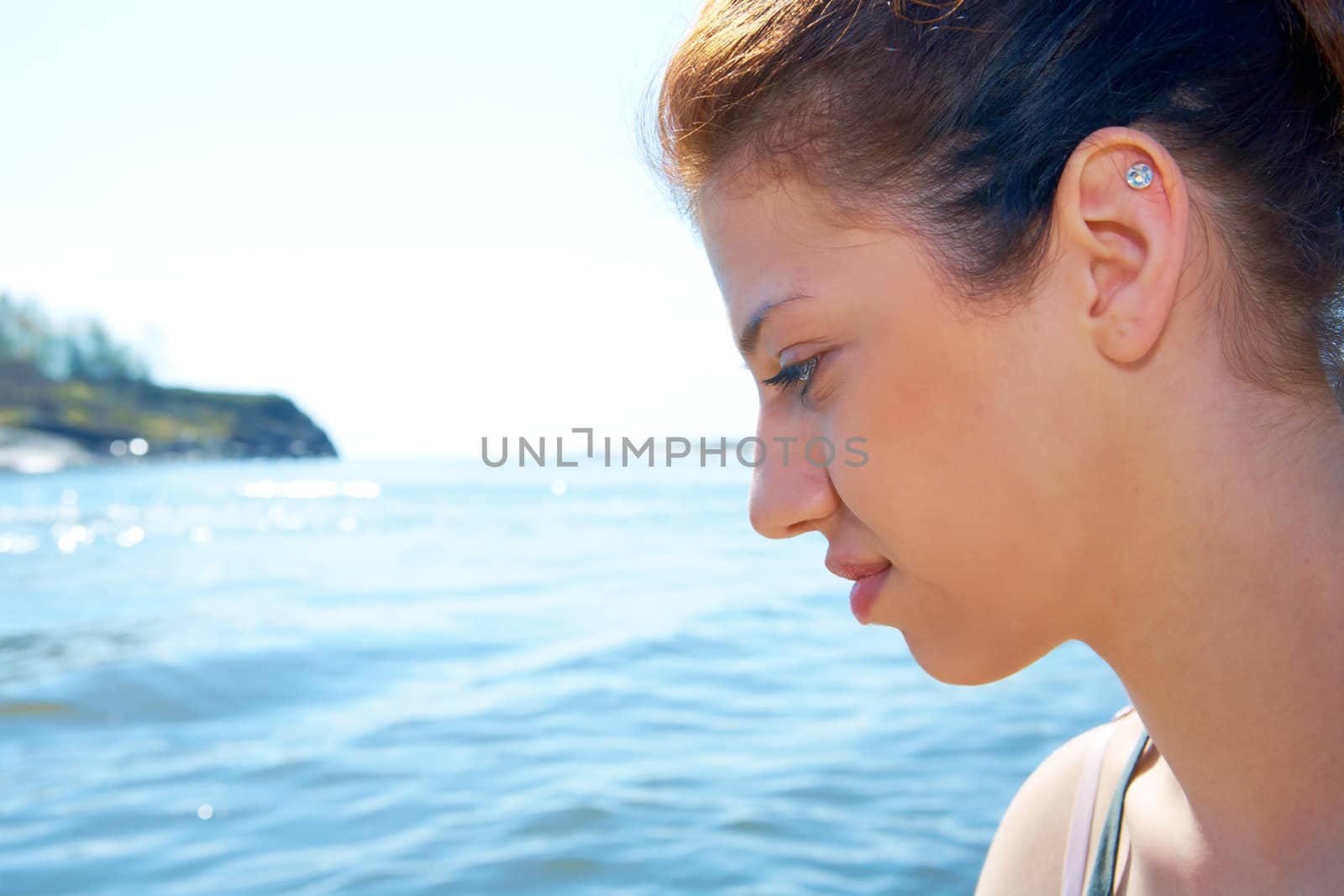 Teenage girl sitting by sea on sunny day side profile