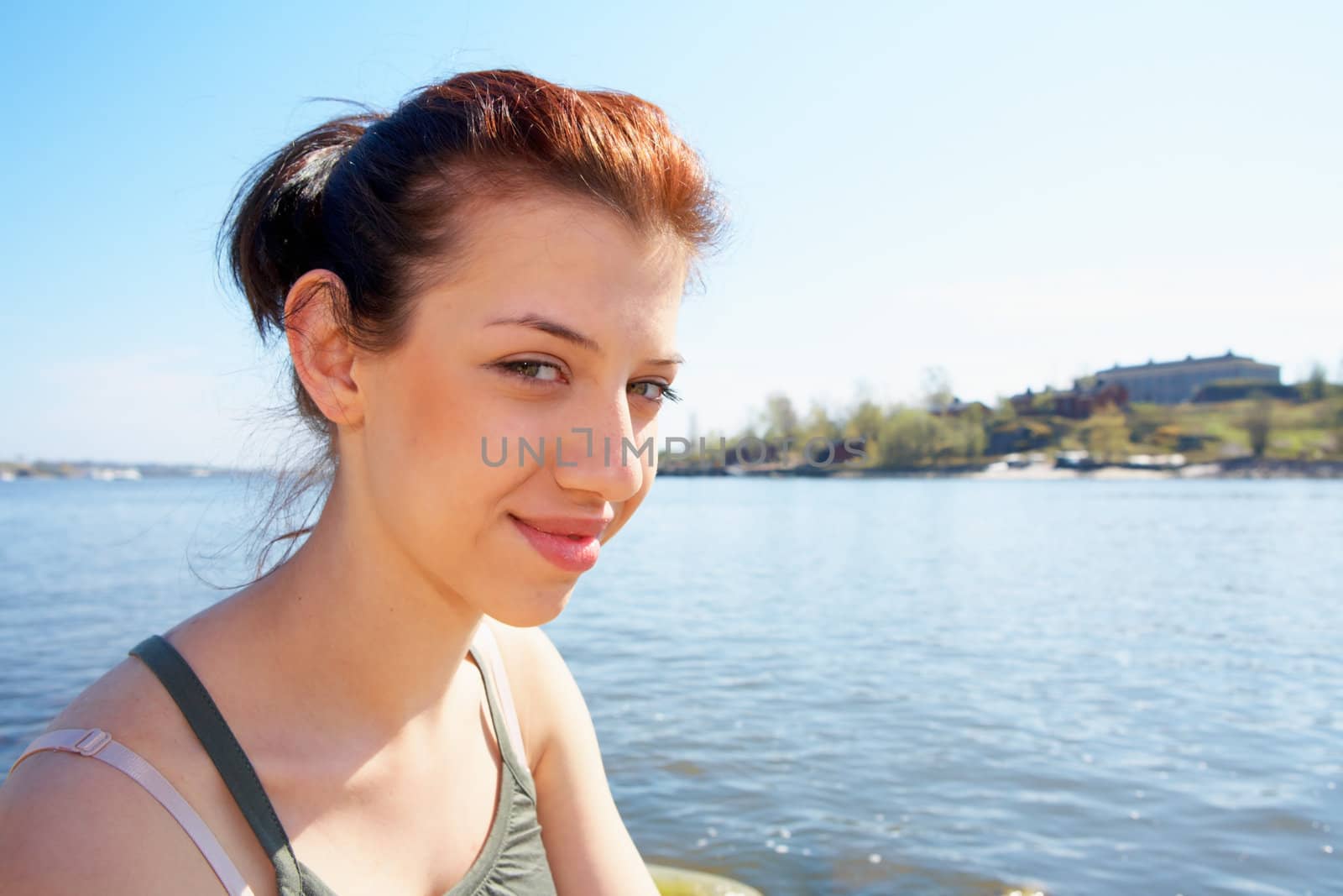 Teenage girl sitting by sea on sunny day looking at camera