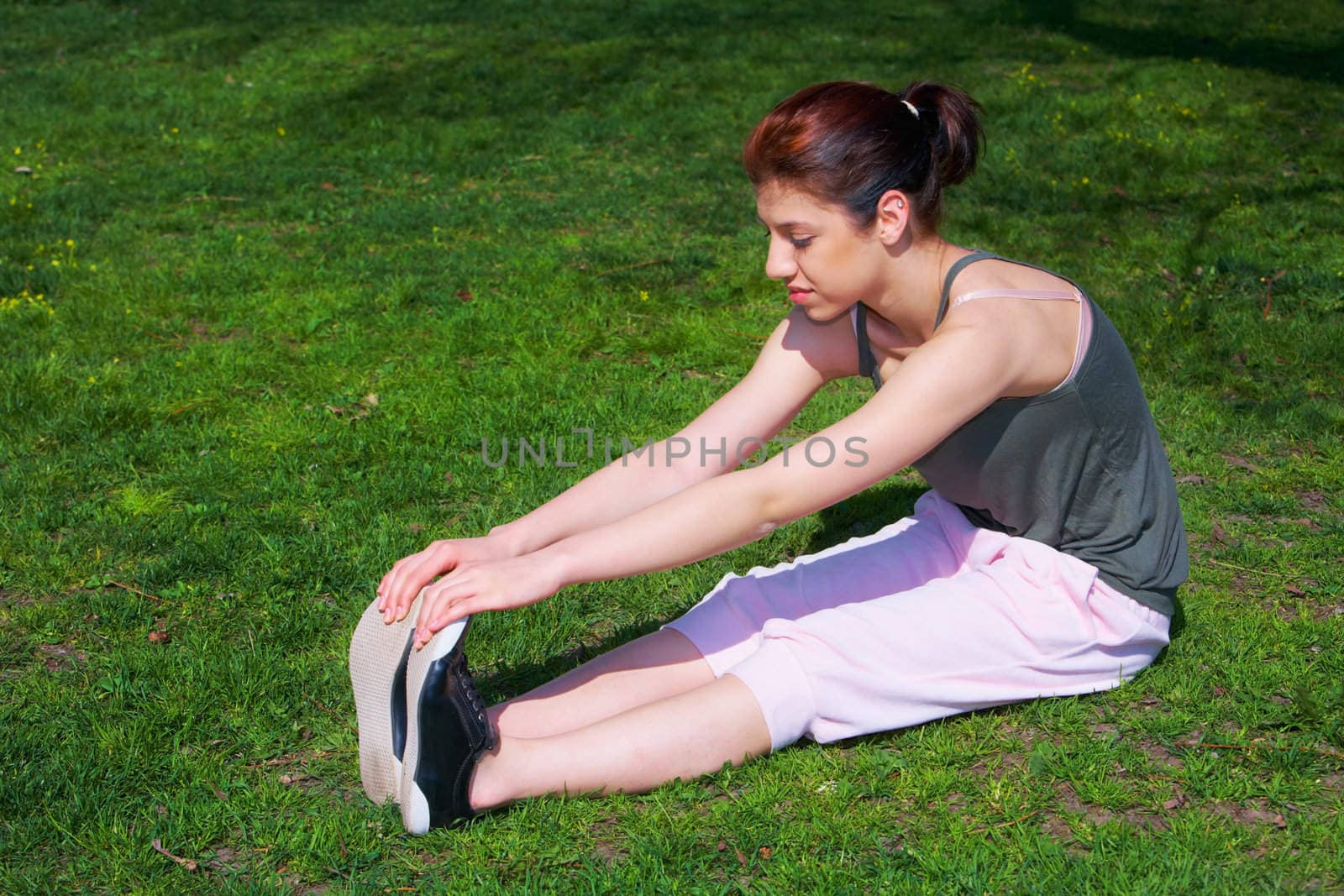 Teenage girl stretching in park, side view