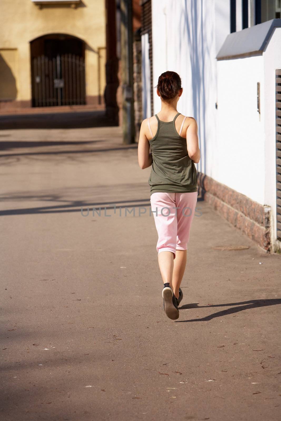 Teenage girl jogging away on sidewalk in city