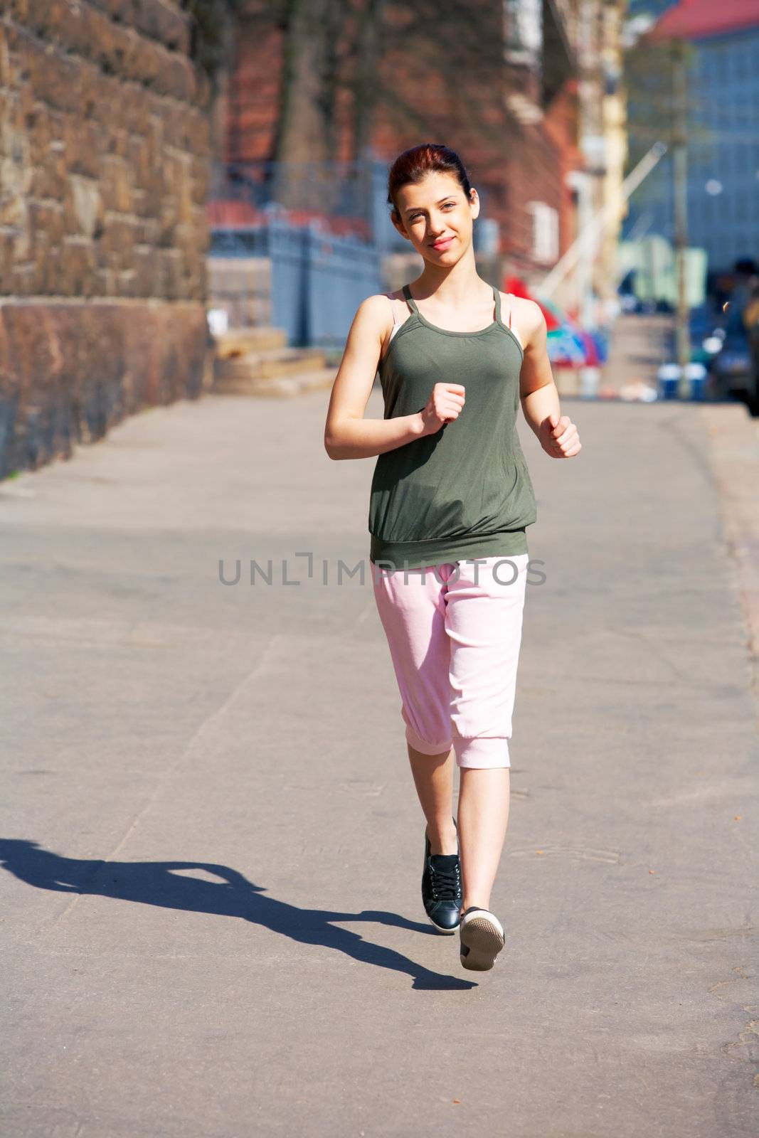 Teenage girl jogging on sidewalk in city, looking at camera