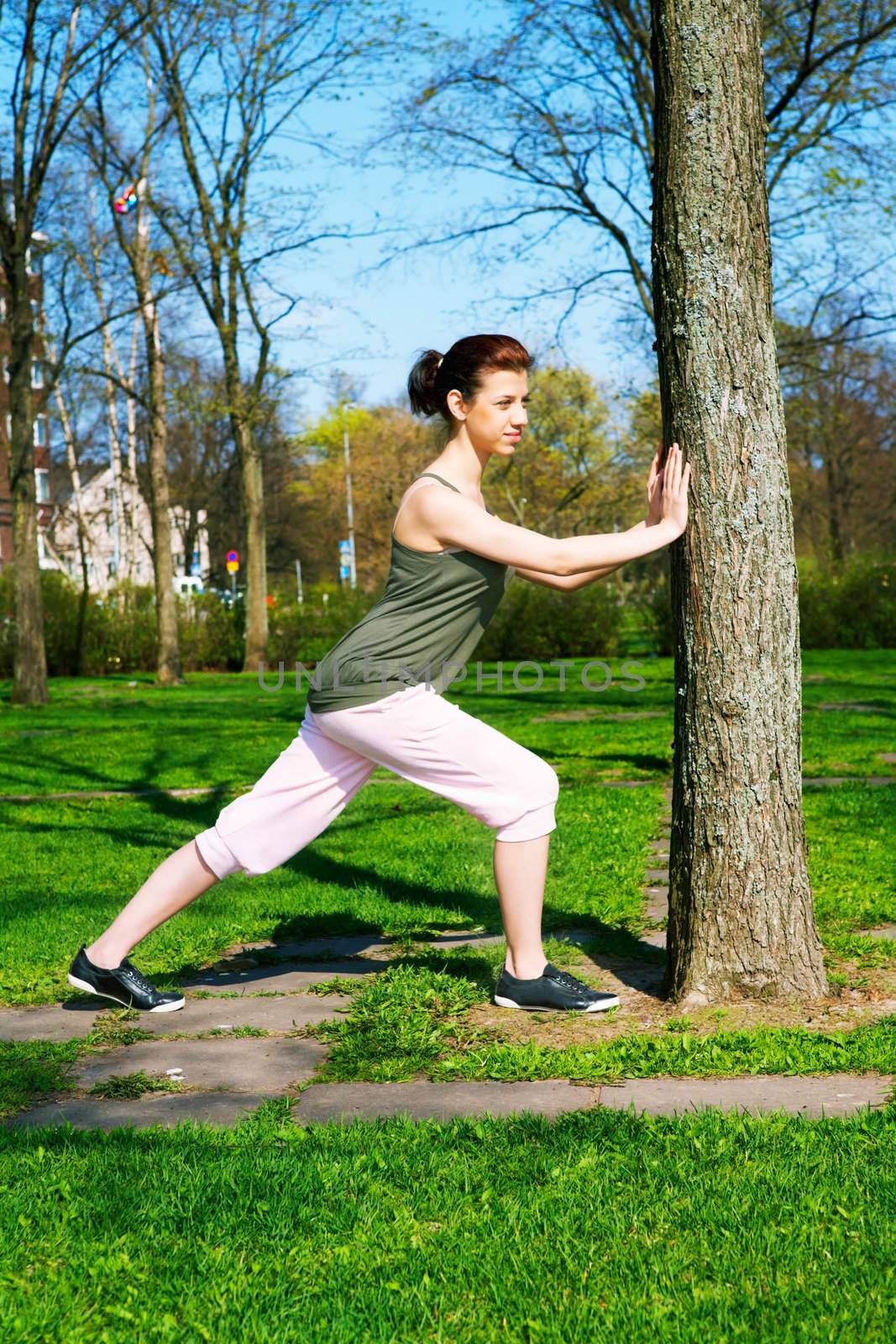 Teenage girl stretching in park in spring