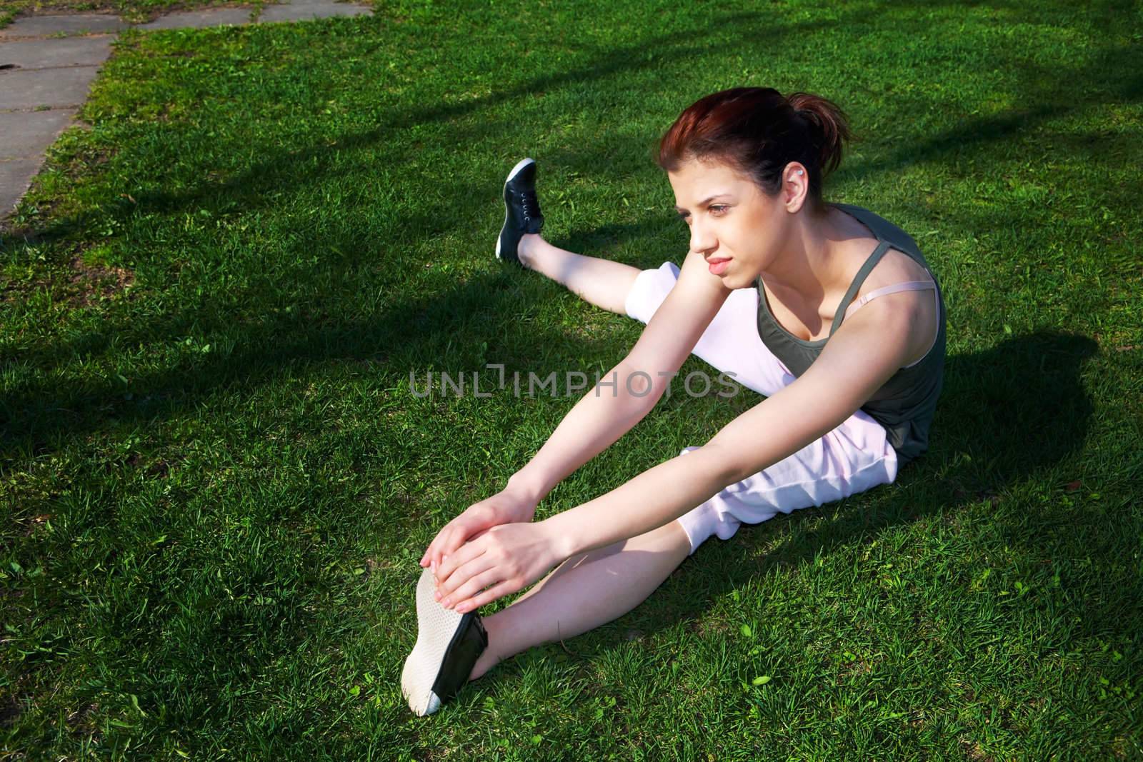 Teenage girl stretching on grass in spring