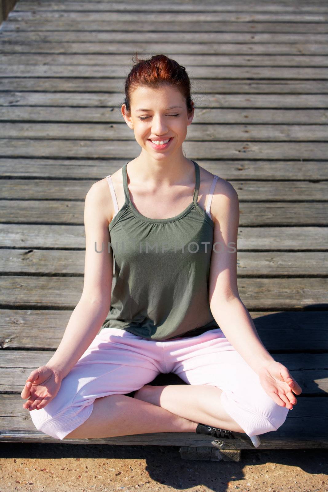 Teenage girl meditating on pier outdoors, smiling