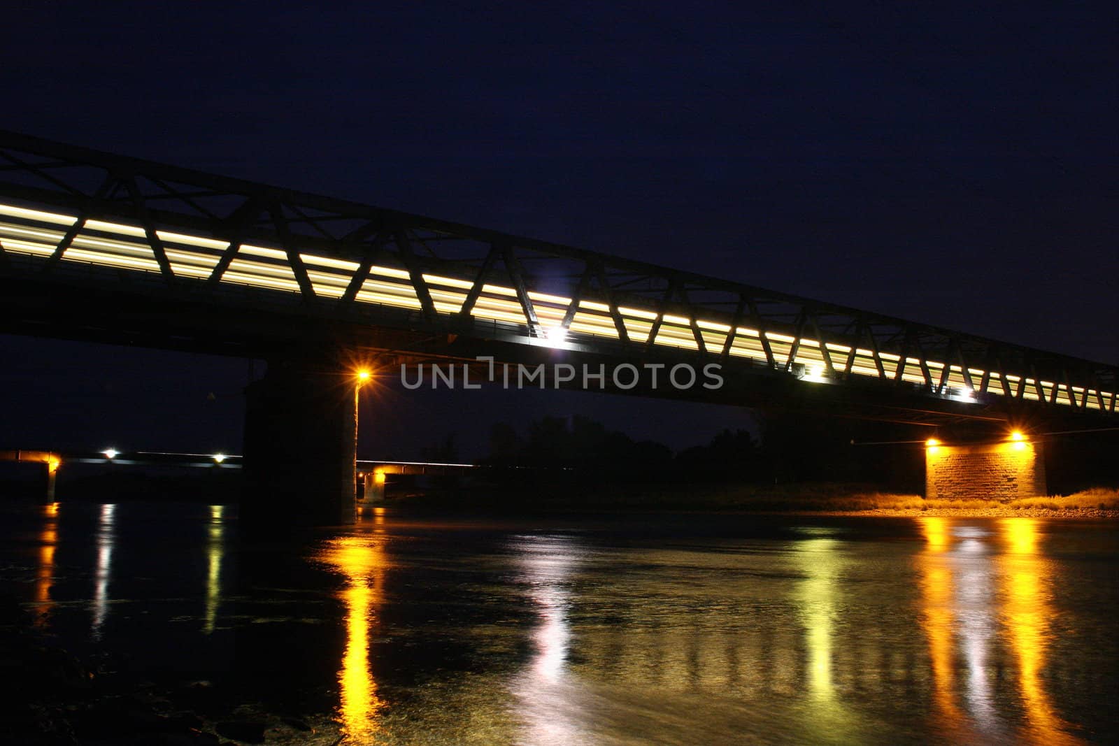 Illuminated railway bridge over the Elbe in Dessau - Rosslau, in Saxony-Anhalt / Germany, with a moving train
