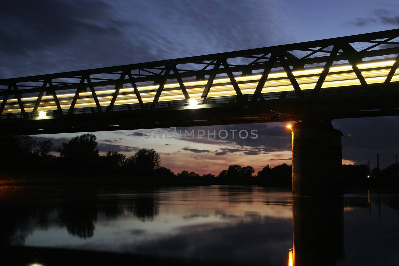 Illuminated railway bridge over the Elbe in Dessau - Rosslau, in Saxony-Anhalt / Germany, with a moving train