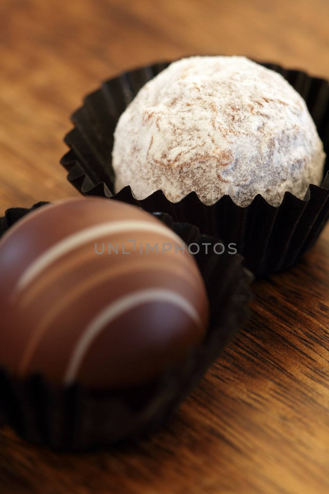 Photo of two chocolate truffles in paper wrappers.  Very Shallow depth of field, focusing on white truffle.
