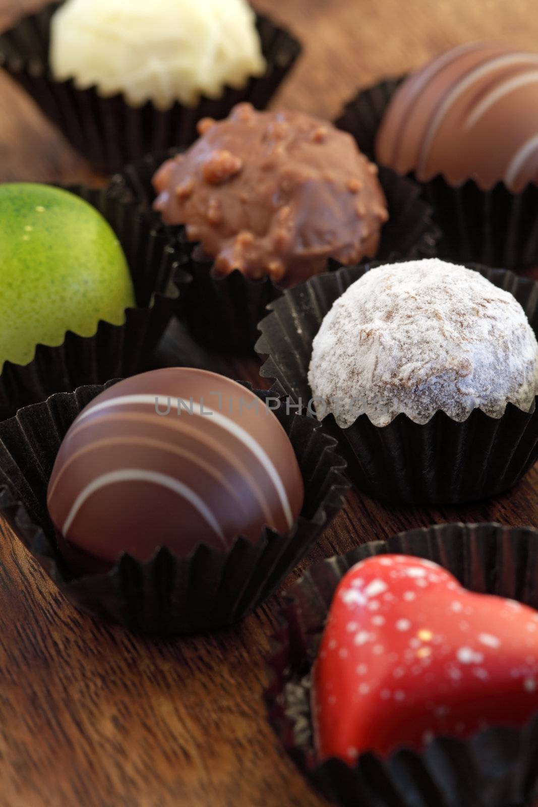 Photo of assorted truffles, pralines, and liqueur filled chocolates in wrappers.  Shallow depth of field focusing on white chocolate.