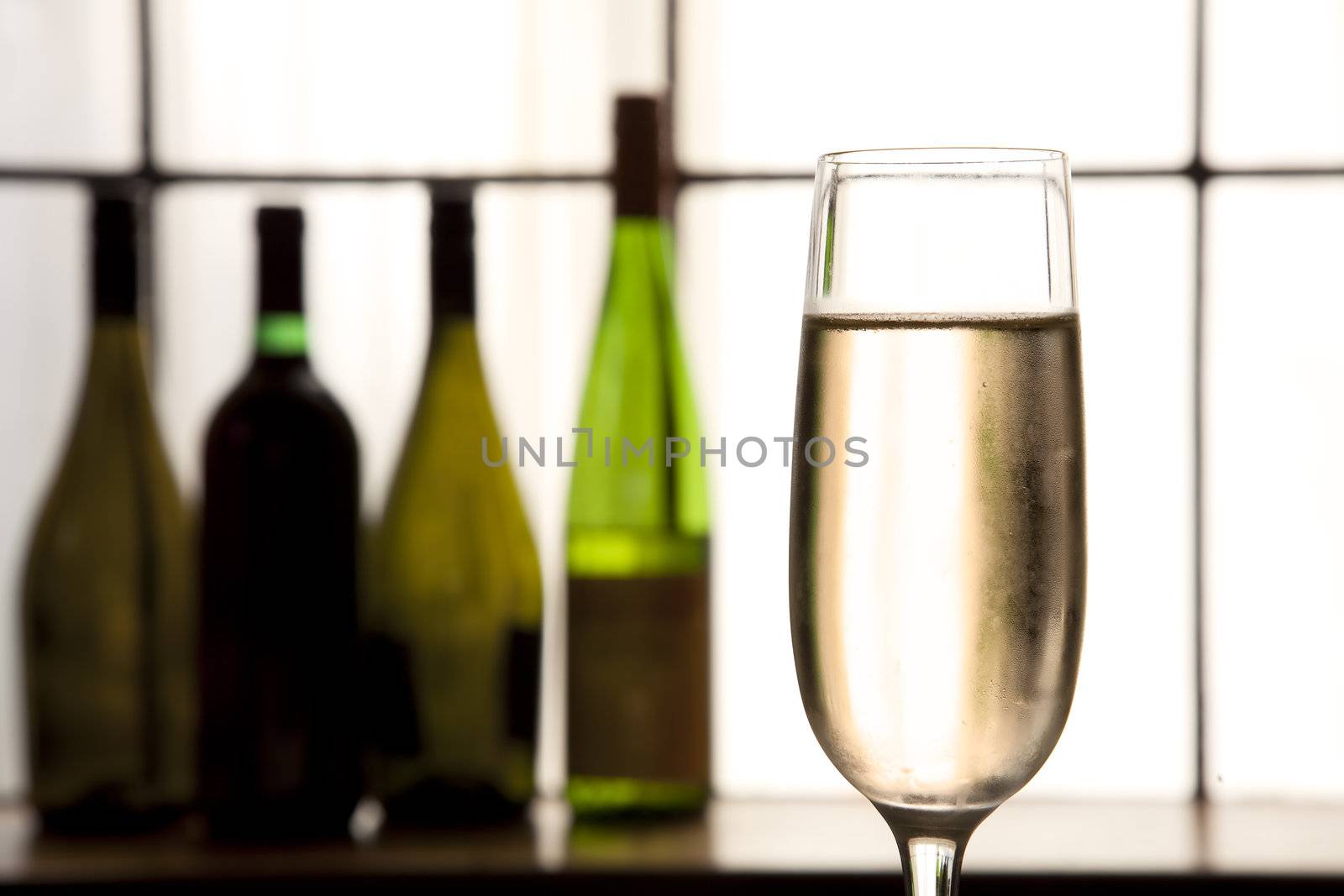Glass of champagne in foreground with sepia tones and bottles in back ground.