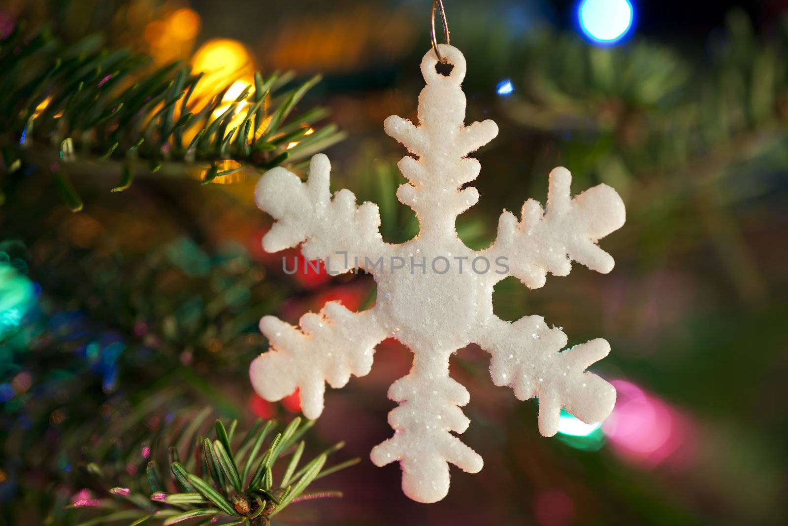 White snow flake Christmas ornament hanging on Christmas tree with out of focus lights.