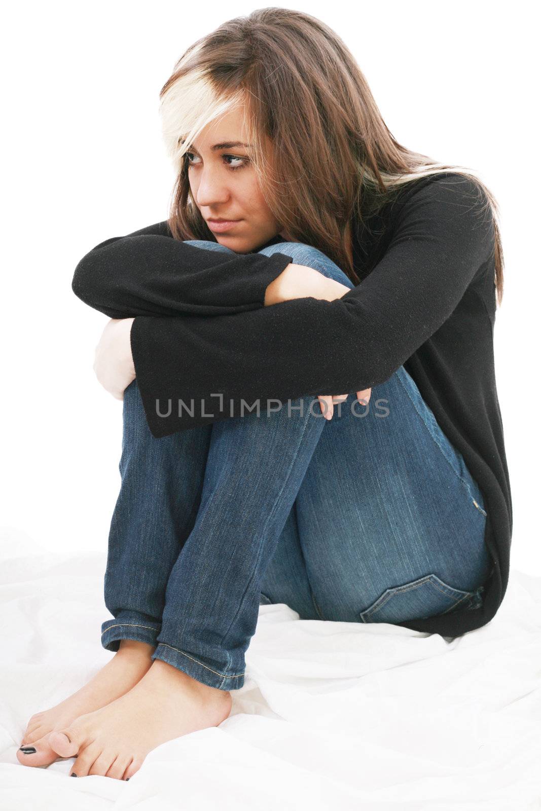 Sad girl teenager sits twining arms about legs. Isolated on a white background.