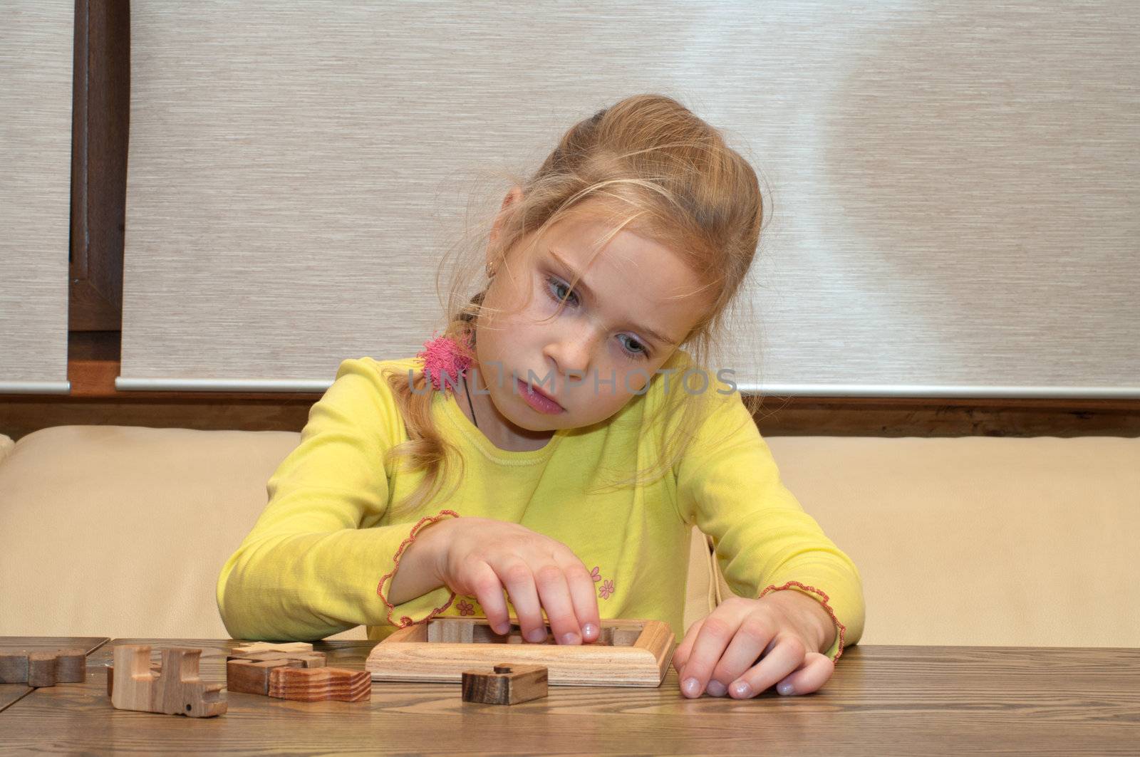 Thoughtful blonde girl collects a puzzle.