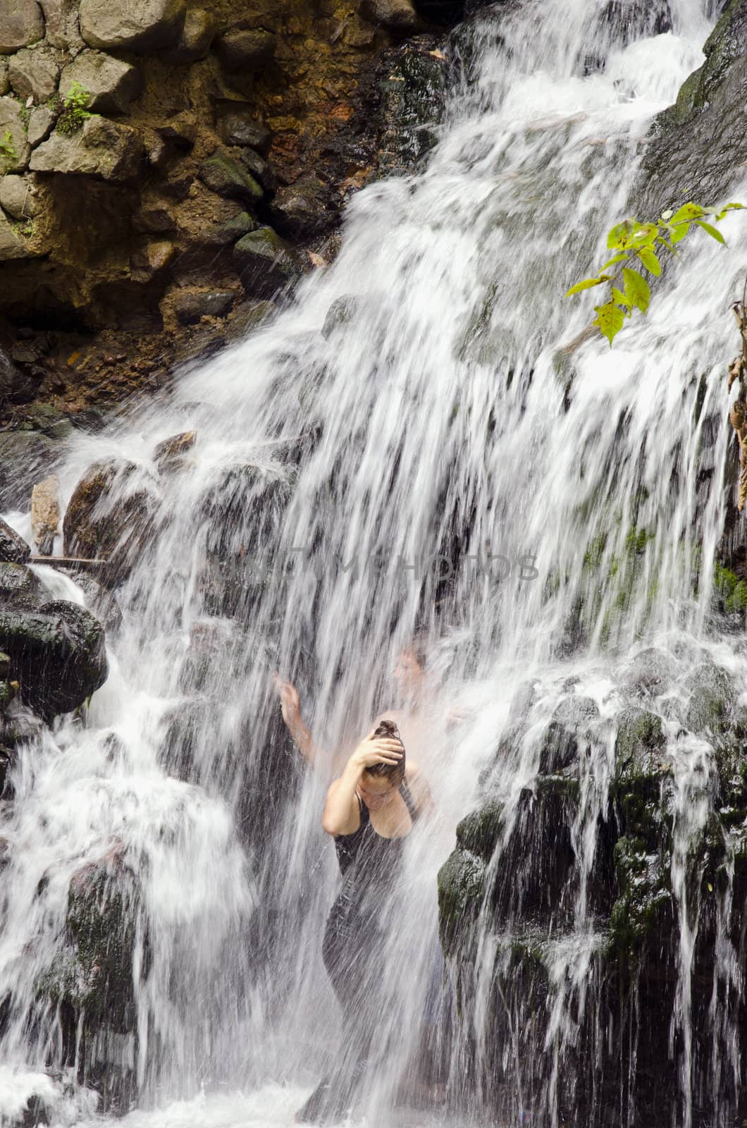 Two youth refreshing under the flow of small waterfall in hot day.