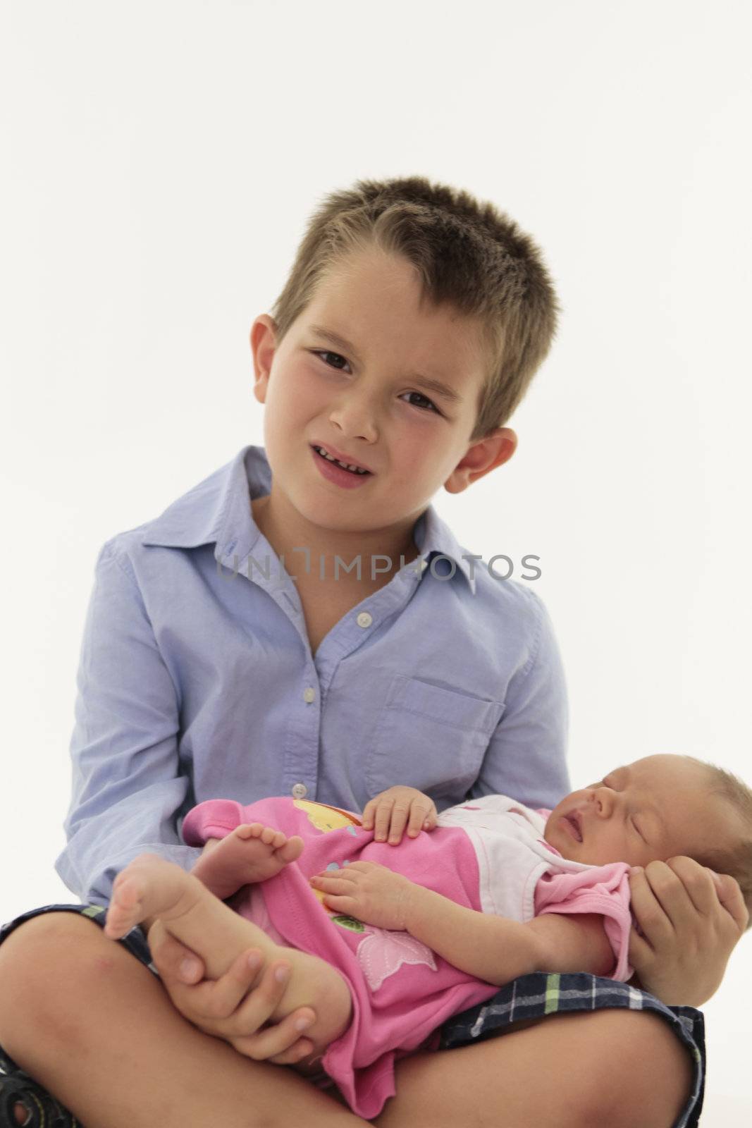 Todler holding newborn baby sister and he has a confused, questioning look on his face.