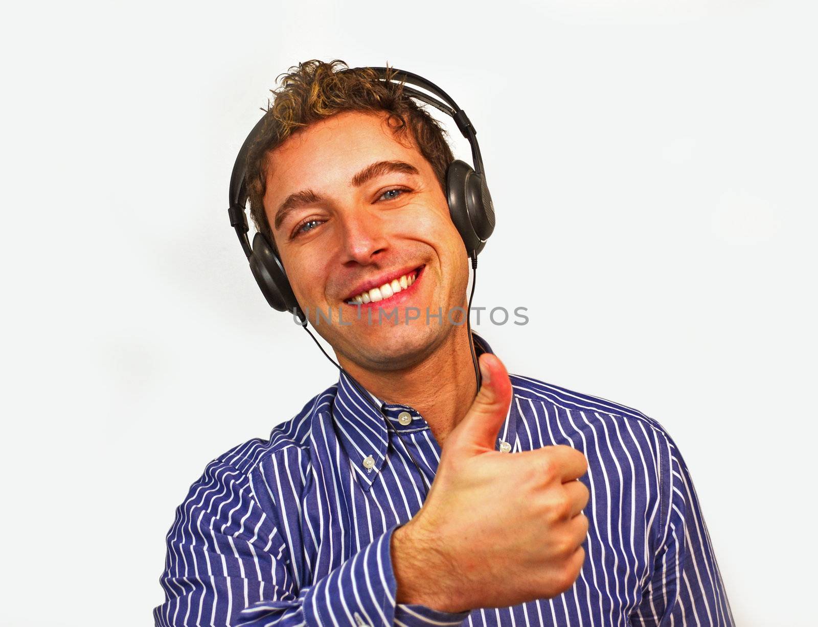 Attractive young man with thumb up and smiling while listening to music through headphones