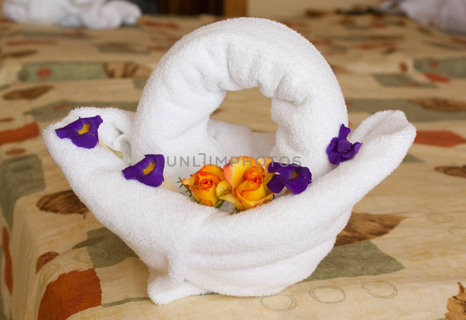 Towel art: towel shaped as basket with colourful flowers inside on a hotel bed.