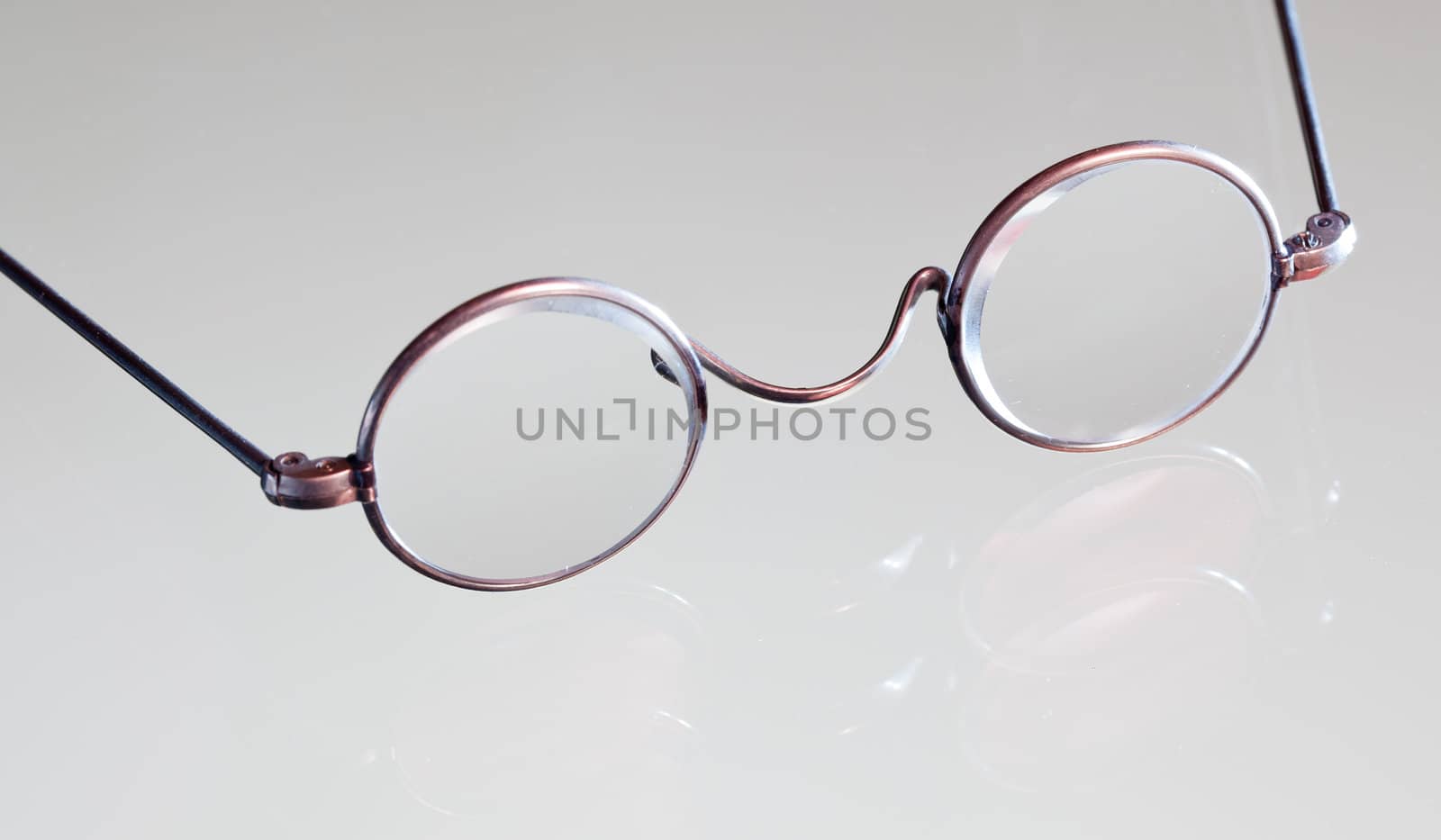 Old fashioned round reading glasses laying on a glass table and reflecting in the surface