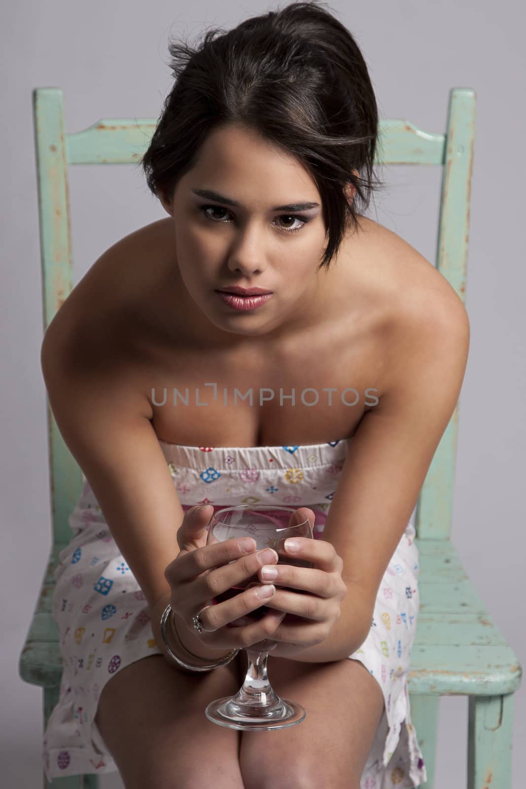 Young woman sitting on a green chair, holding a glass of wine, looking straight at the camera