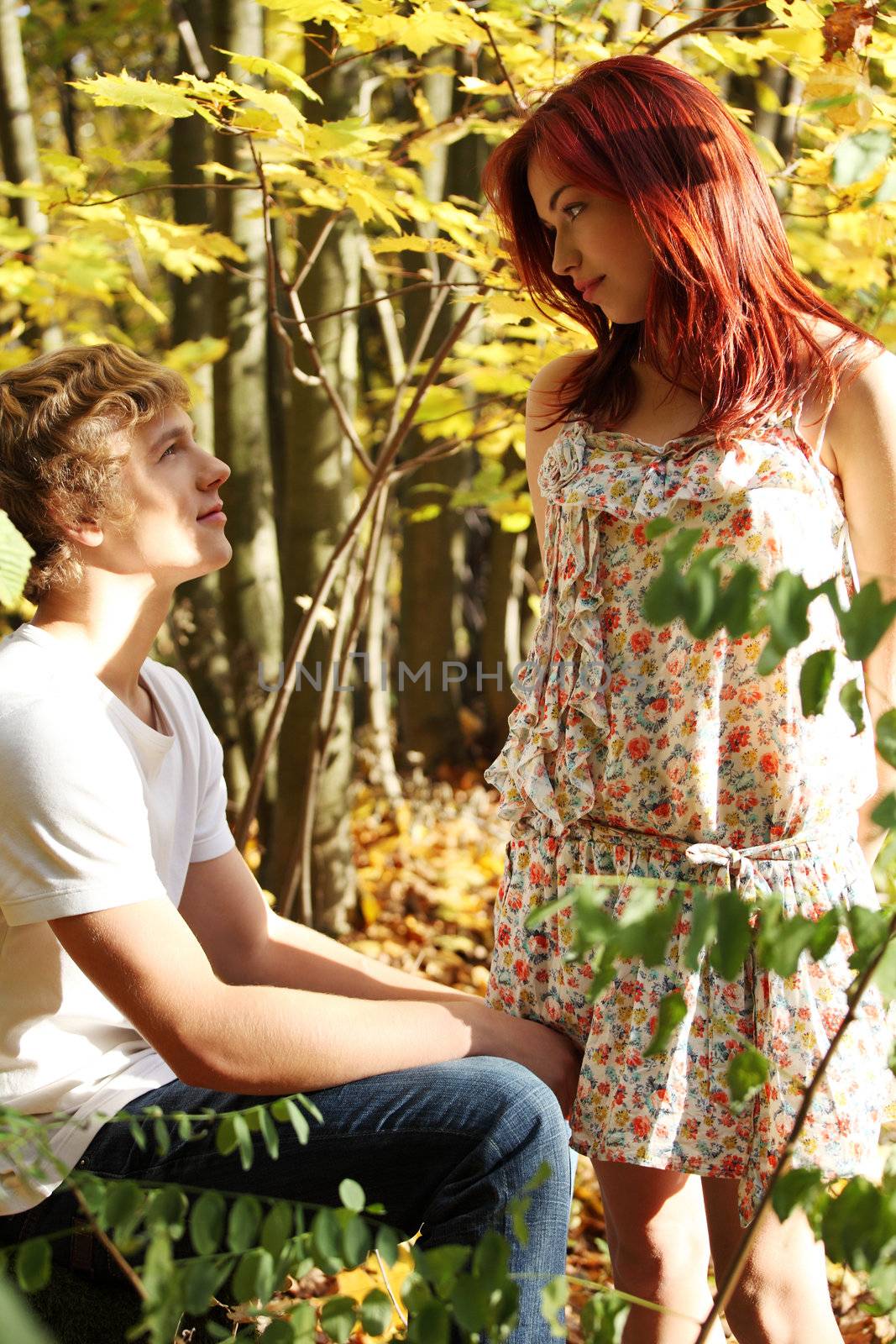 Handsome caucasian boy sitting down with girl standing and looking in his eyes.