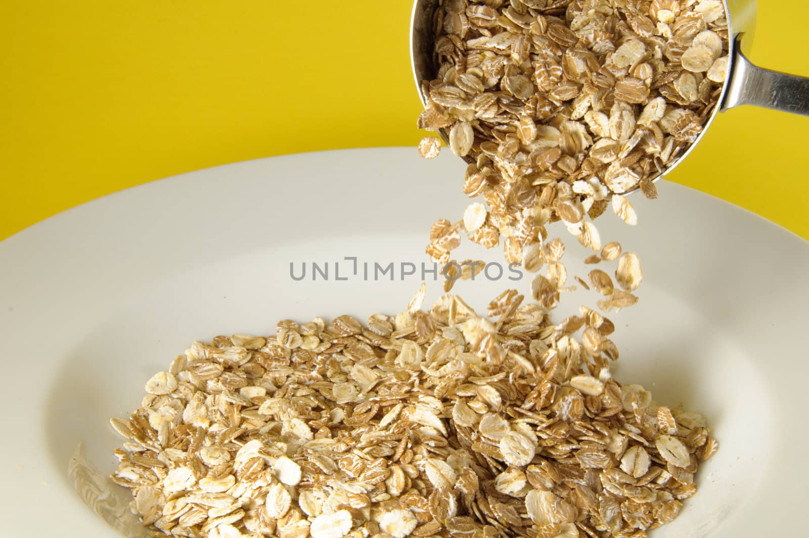 Measuring cup pouring organic cereal on white plate over colorful yellow background