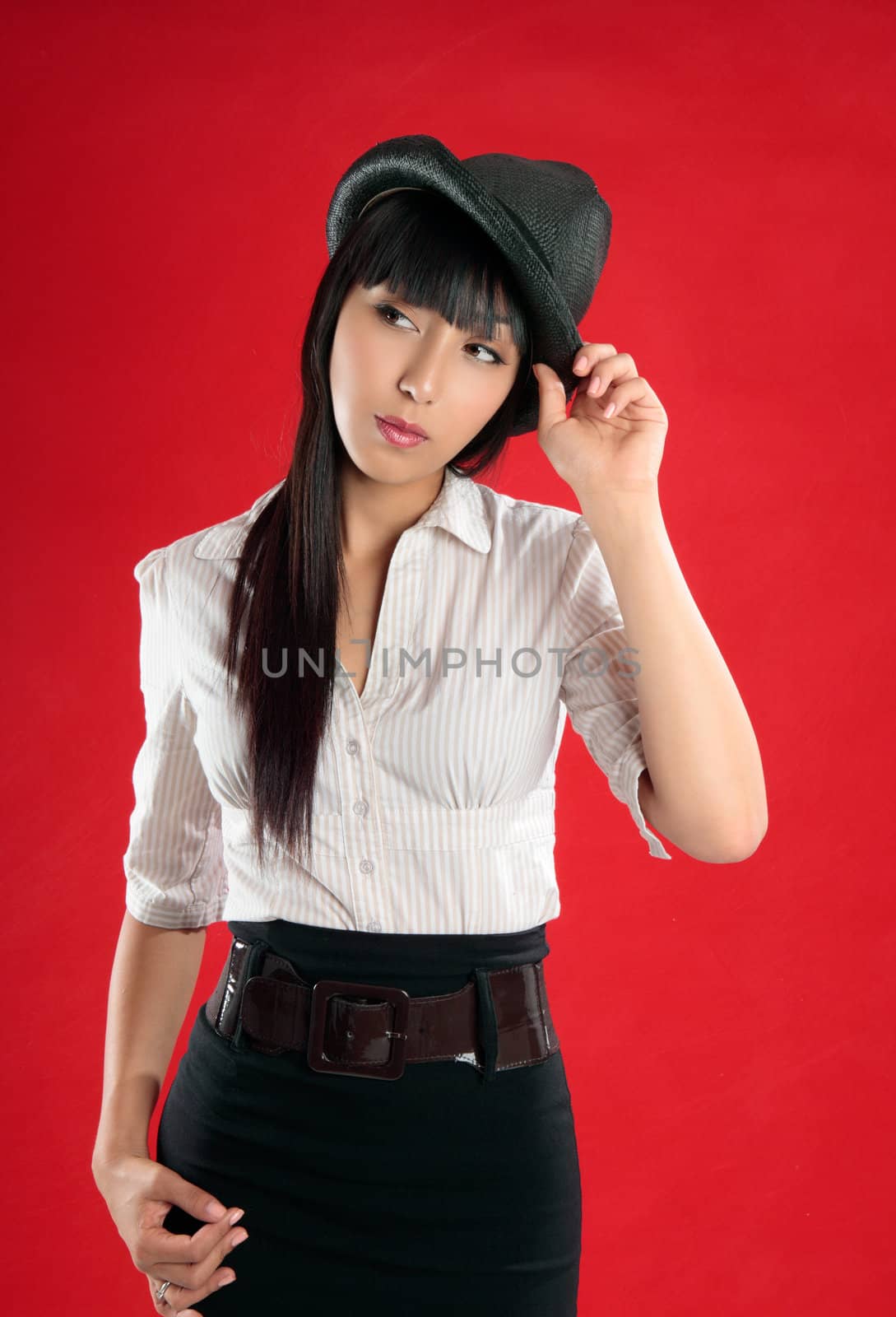 Young pretty woman wearing a beige white striped blouse, black skirt and hat.  She is looking sideways and is tilting her head slightly.